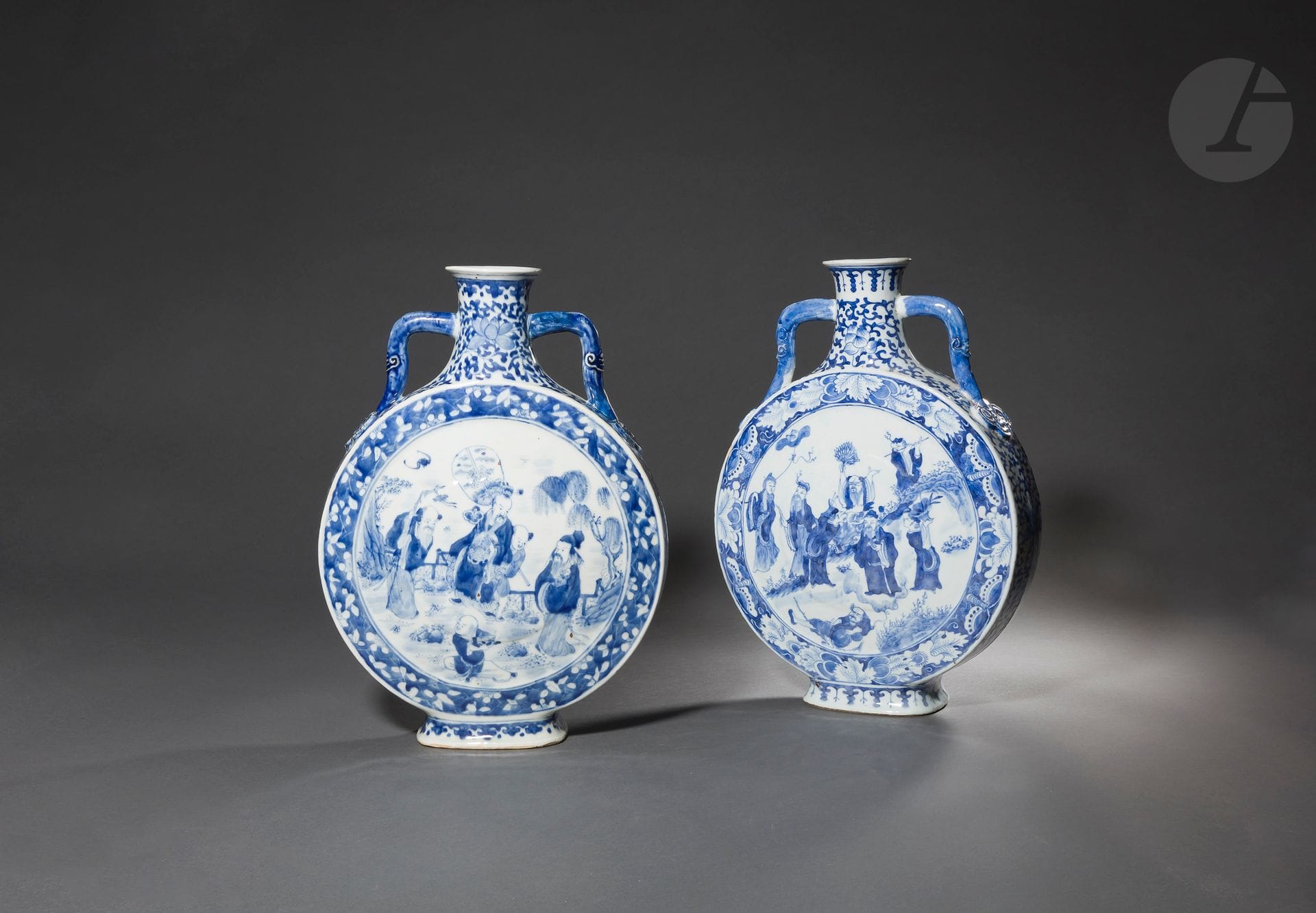 Paire de gourdes de type bianhu - 扁壶 en porcelaine émaillée bleu sous couverte, Chine, XXe siècle
Les gourdes, rondes et aplaties, sont décorées dans des médaillons entourés d’une frise florale, de plusieurs Immortels taoïstes dans des jardins arborés au-dessus desquels volent des chauves-souris, une grue et où apparaît le soleil dans des nuages. Les cols hauts et évasés à décor de fleurs de lotus sur fond de rinceaux sont flanqués d’une anse de chaque côté en forme de ruyi. Au centre de chaque côté des panses, apparaît moulée en très léger relief la forme d’une pêche de longévité.
Hauteur : 40 cm

二十世纪 - 青花颈莲花纹腹八仙人物图如意耳扁壶一对



