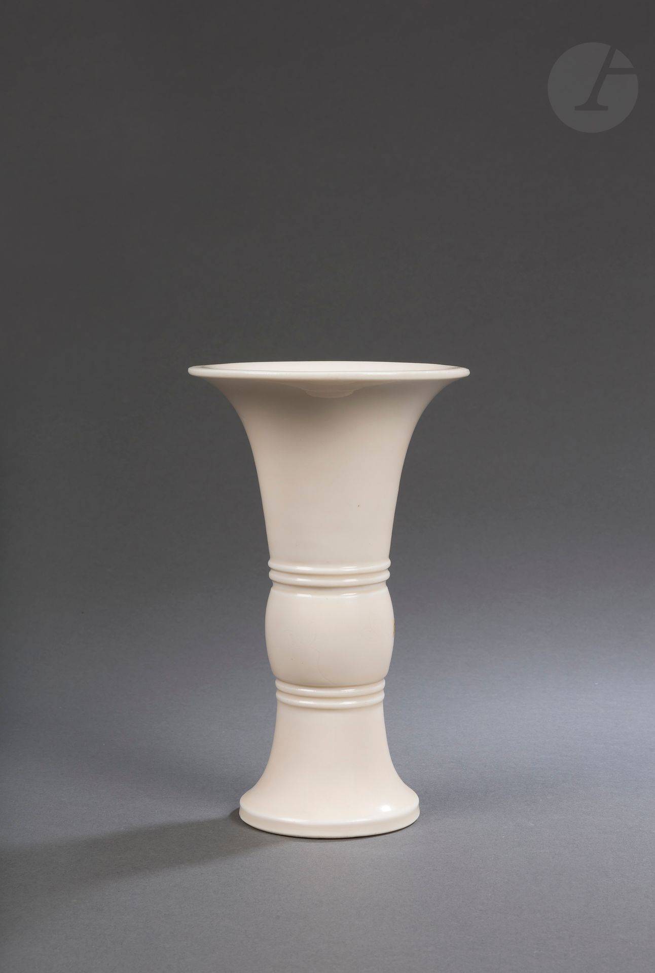 Vase gu en porcelaine Blanc de Chine, Dehua, Chine, époque Kangxi (1662-1722)
De forme inspirée des bronzes archaïques, la partie médiane est formée par un bulbe cylindrique inséré entre deux anneaux en relief et incisé de deux fleurs et une feuille de lotus. Belle couverte de couleur ivoire. Le talon est laissé cru et le dessous émaillé. Socle en bois.
Hauteur : 21,7 cm
Dans une boîte orange.

Provenance : 
Étiquette « 23 juin 1981, n°279 ».

清 康熙 - 德化窑白釉弦纹划花花觚

Collection particulière parisienne - lots de 78 à 127, 219 et 220