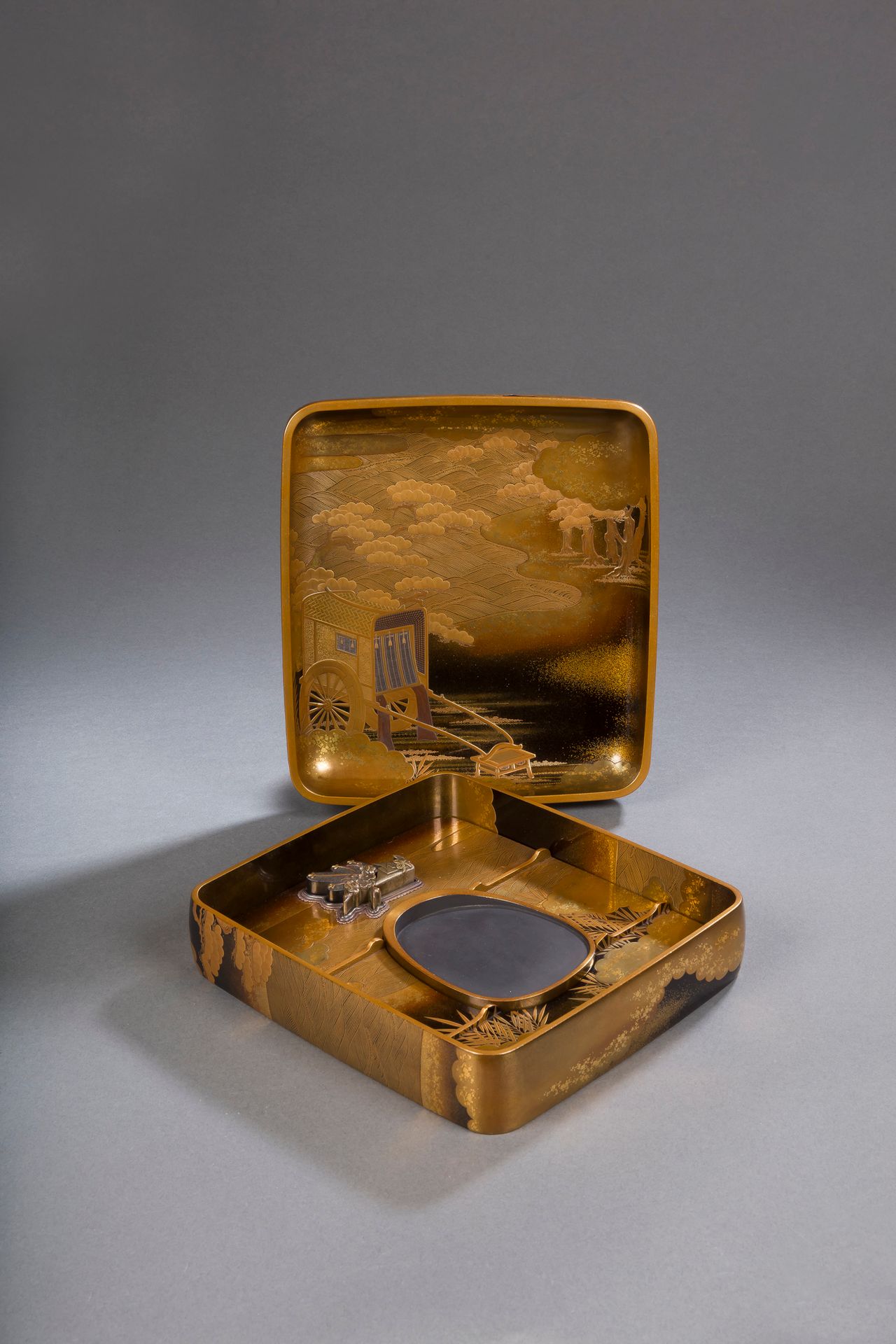 Suzuribako, Nécessaire à écrire, Japon, époque Meiji (1868-1912)
En bois laqué à fond ro iro et mura nashiji à décor en hiramaki-e, takamaki-e or et argent et kirigane d’un torii à l’entrée d’un taiko bashi ou pont tambour, entouré de pins, de vaguelettes écumantes et de nuages. L’intérieur du couvercle à décor dans les mêmes techniques d’un gissha (牛車 - char à bœufs utilisé pour le transport des nobles à l’époque Heian, probablement d’origine impériale puisque l’on aperçoit un décor de chrysanthèmes sur les côtés) entouré dans le même environnement de pins, de nuages et de vaguelettes. L’intérieur de la boîte contient un suzuri-ishi en bois laqué, un mizu-ire en alliage de cuivre patiné à décor d’un noshi (origami traditionnel faisant office d’enveloppe à l’occasion de fêtes) contenant des branches de jeunes pousses de pins et une autre de branches de pruniers en fleurs, symboles de longévité que l’on s’offre pour la nouvelle année. Le dessous du suzuri bako à décor en hirameji sur fond ro iro, de même que le suzuri-ishi. Le décor du couvercle est en continuité sur les bords du suzuribako.
5,5 x 23,5 x 22 cm
Avec une boîte en bois.

Provenance : 
Étiquette sur la boîte en bois Swedish cat number 71.

Collection particulière parisienne - lots de 78 à 127, 219 et 220