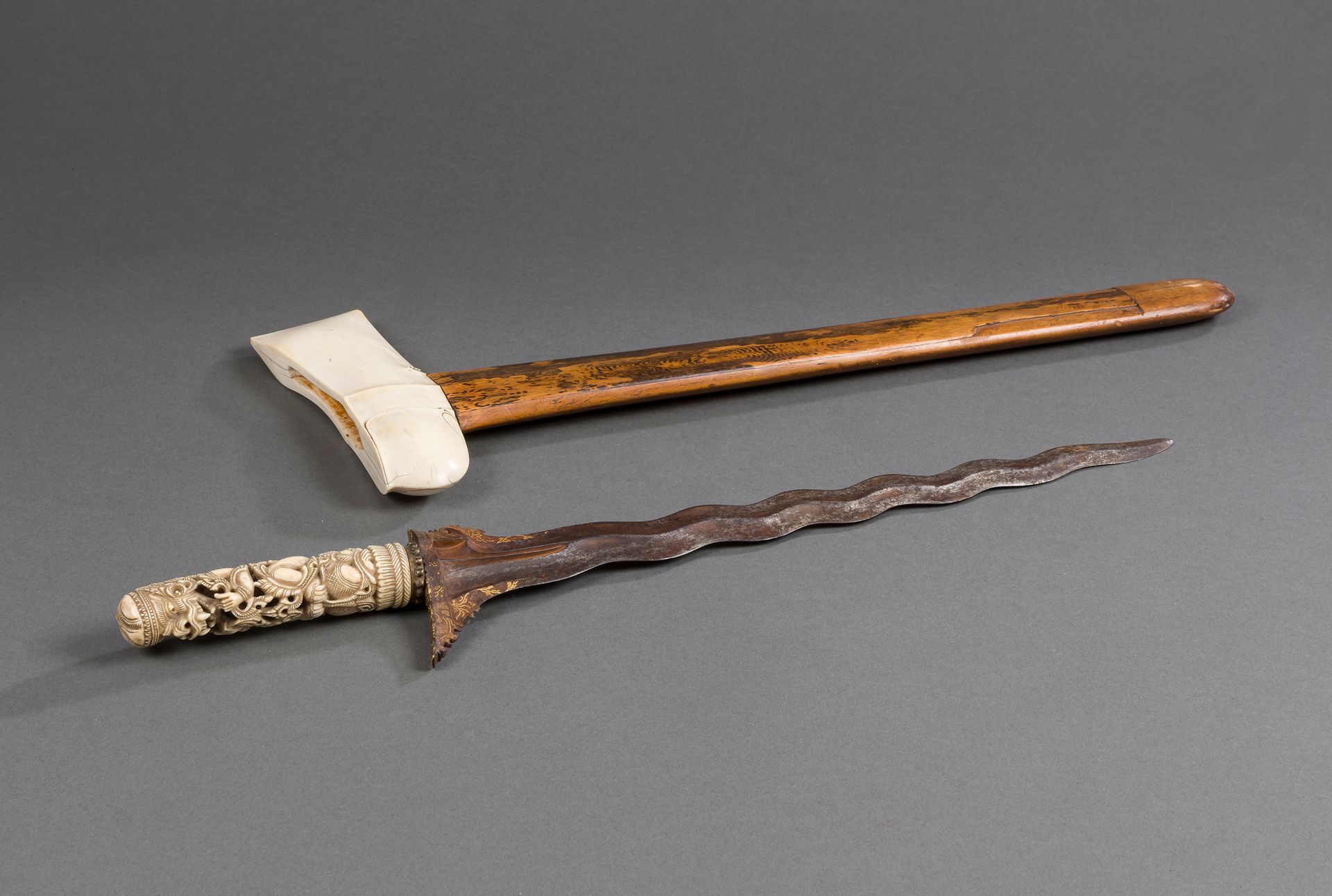 Kriss (kris or keris) with wood and ivory mounts, Indonesia, Bali or Kadutan, 19th - 20th century
It consists of a hulu or ukiran handle in openwork ivory representing a terrible deity, probably Barong. The wilah blade, made of iron alloy forged according to the pamor technique (damascus style), is made of an odd number of concave curves, the luk, as is the rule. The top of the blade is gold damascened with a floral decoration and the flat of the ganja (flat of the top of the blade) is inlaid in brass with floral scrolls. The warangka or sarung scabbard is made of several types of wood and the upper part of ivory.
Length : 61 cm ; weight : 584 g
CIC permit n°FR2307503660-K

