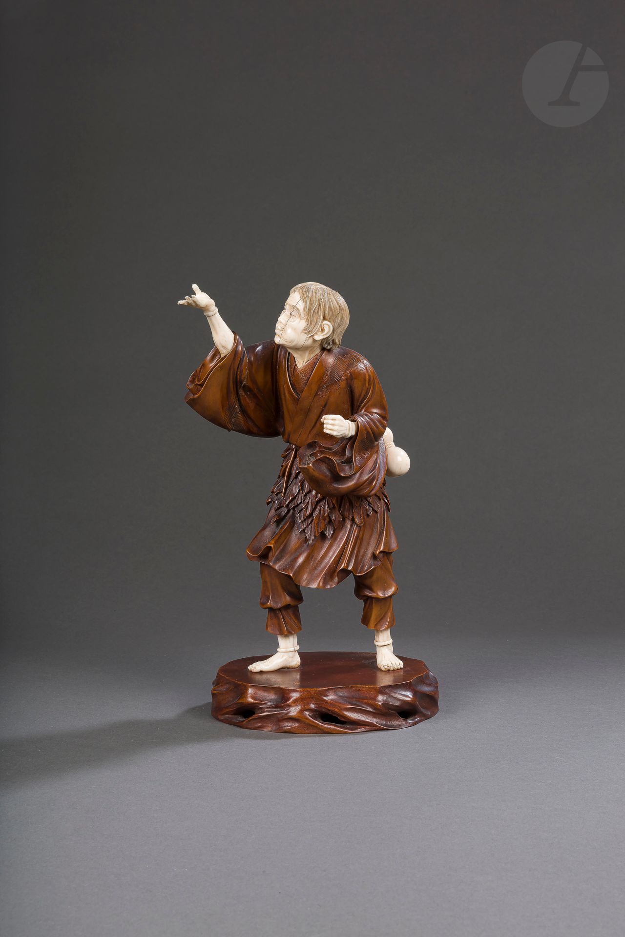 Wood and ivory Okimono representing Tekkai sennin (Li tieh kuai in Chinese), Japan, Meiji period (1868-1912)
The head, the right forearm, the hands and feet as well as the gourd are made of ivory while the rest of the body is made of wood. He is looking at his open hand palm upwards from his raised right arm. His cheeks are puffy and he seems to be blowing towards his hand. In his other hand he is holding a gnarled stick that has disappeared. He is dressed in a worn garment with a leafy border around his waist, typical of sennin representations, and wears a coloquint on his belt that serves as a gourd. He is standing on a wooden base fixed by two brass screws. Under this base a red stamp with the signature Ryôun - 竜雲.
Height: 28 cm; gross weight: 916 g
CIC permit n°FR2307503661-K
Gerce with face.

