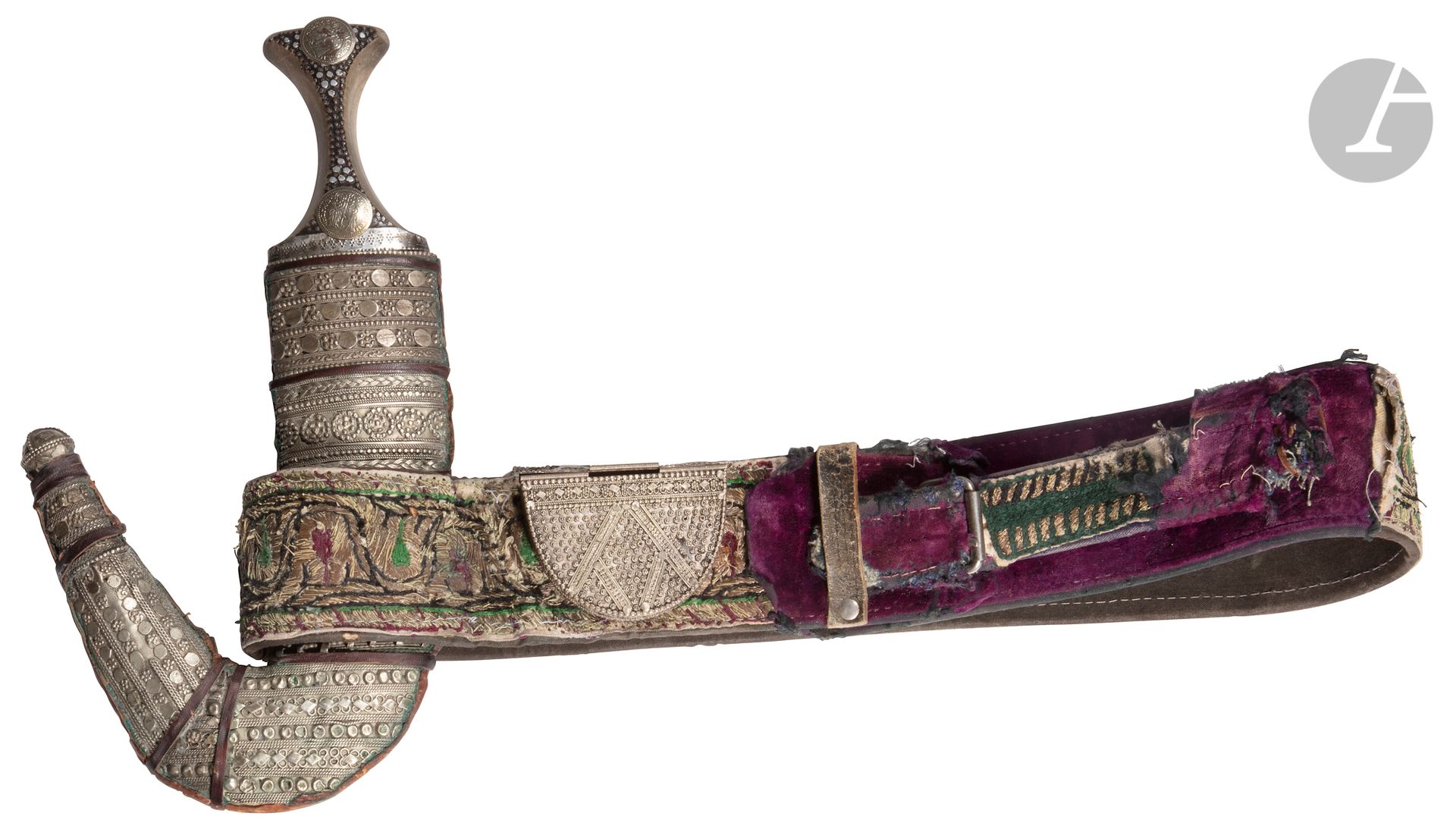Jambiyya dagger and belt, Yemen, 19th century
Curved blade with steel center rib, horn handle with studded decoration and two silvered metal medallions imitating coins of the Republic of Venice riveted. Wooden scabbard sheathed in leather and lined on one side with metal plates with beaded, braided and chased geometric decoration. The scabbard is mounted on a nylon belt lined with purple velvet, embroidered with metallic threads and polychrome cotton and decorated with small talismanic boxes and a silver bottle. 
Length of the dagger : 30,5 cm ; size of the belt : 6,7 x 105 cm
Traces of rust on the blade, damaged belt, some traces of oxidation on the sheath.

Provenance: 
According to family tradition, set given by the brother of the Emir of Yemen to the current owner. 

A Yemeni Horn-hilted Jambiyya Dagger, 19th century