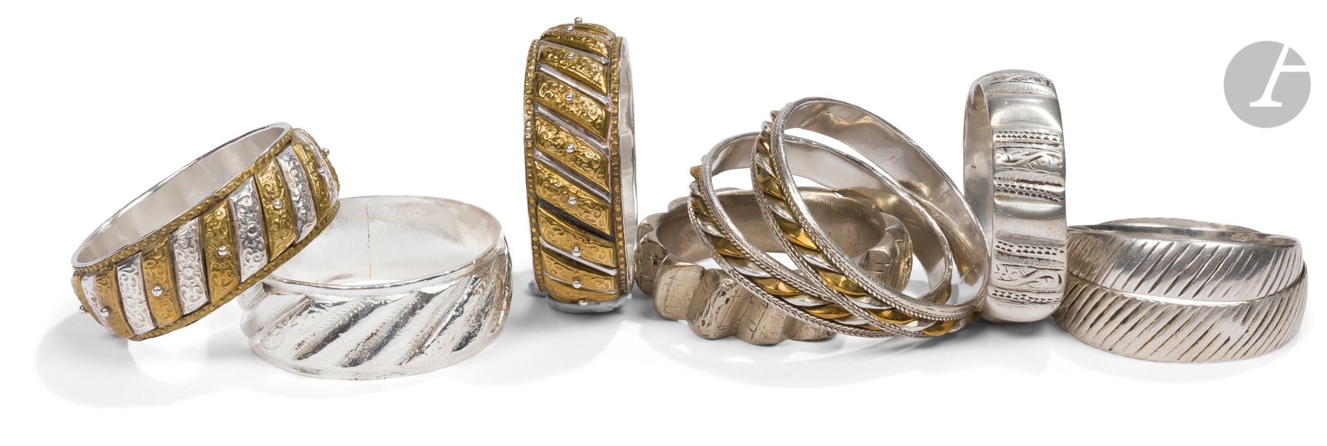 Neuf bracelets godronnés dont quatre shams-u qamar, Nord du Maroc, XIXe - XXe siècle
Sept en argent, quatre bracelets shams-u khamar (lune et soleil) dont deux fins formant paire, partiellement dorés à godrons moulés et gravés d’un décor floral, encadrés de frises perlées ou tressées, deux bracelets à décor gravé de stries obliques, un à godrons alternativement lisses ou gravés, un en métal argenté à godrons, un dernier en métal fortement dentelé au profil étoilé.
Diamètre : 6,3 à 7,5 cm ; poids brut : 655 g
Un bracelet réargenté.

9 Knurled Silver and Metal Bracelets including 4 Shams-u Qamar, North Morocco, 19th - 20th century