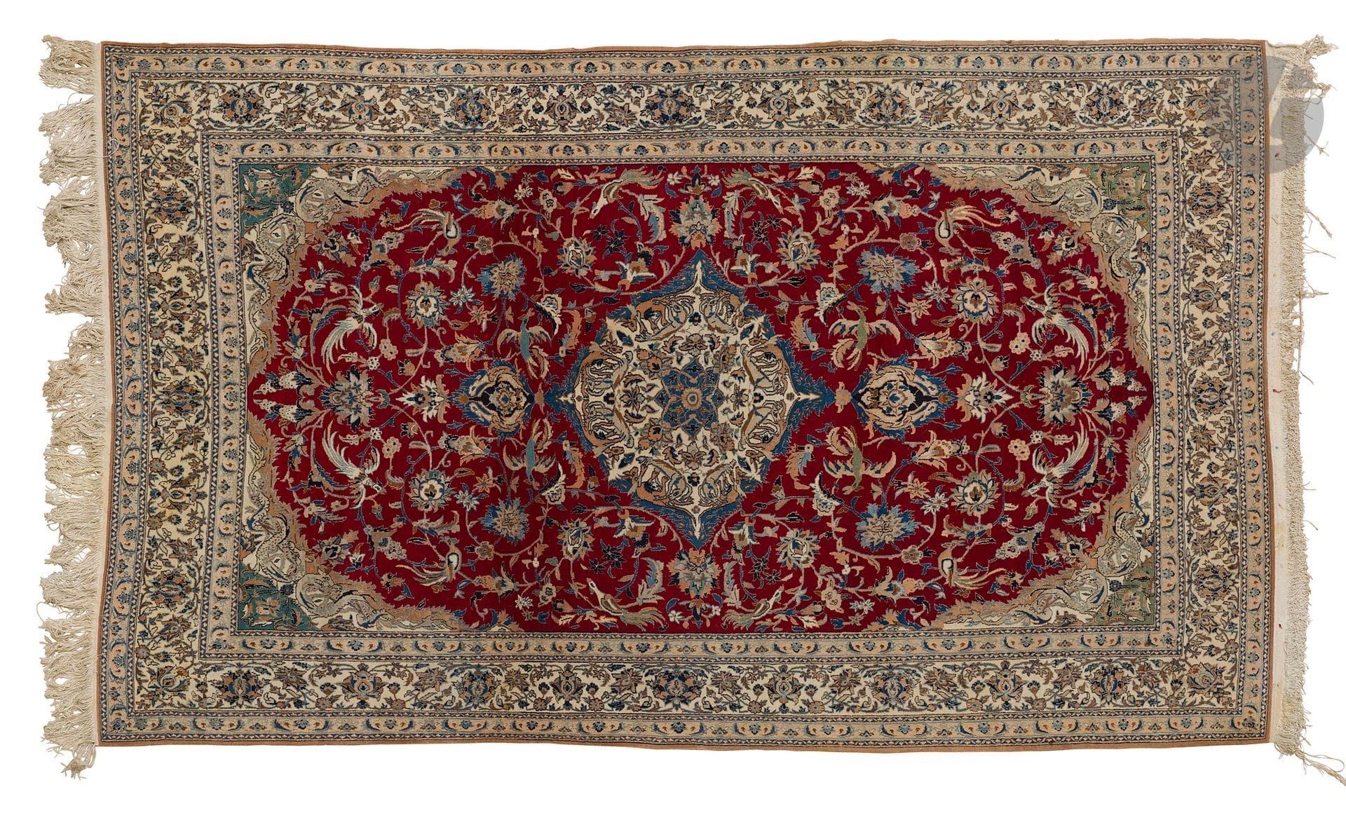 NAIN, XXe siècle, velours laine et soie (5%), chaînes et trames coton.
Tapis à médaillon central ivoire et bleu sur un fond rubis à rinceaux fleuris et volatiles, bordure ivoire à guirlandes de fleurs. 
189 x 310 cm