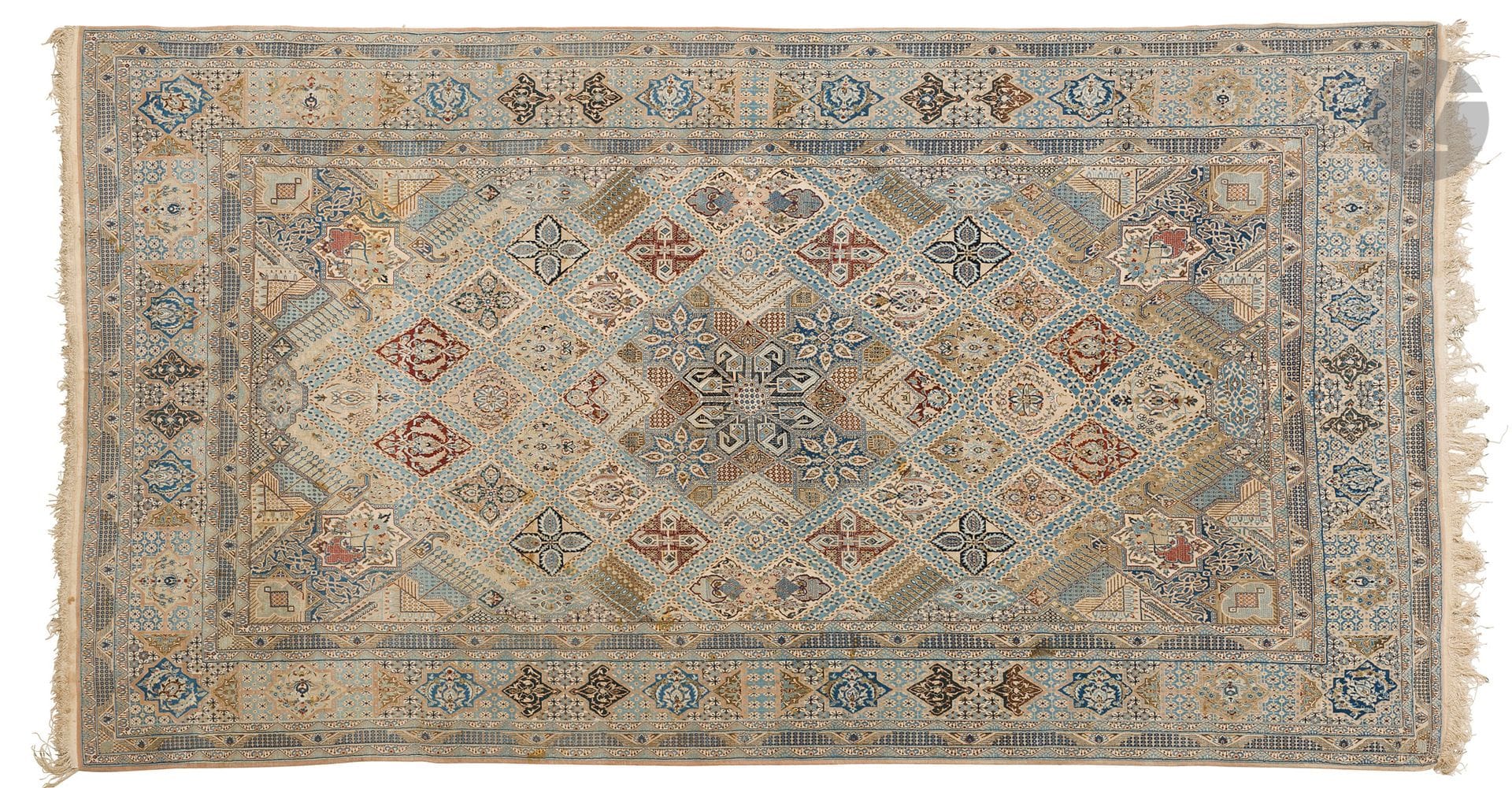 NAIN, XXe siècle, velours laine, chaînes et trames coton.
Tapis à décor de multiples losanges agrémentés de bouquets de fleurs sur un fond bleu clair, large bordure à dessins géométriques répétitifs. 
394 x 216 cm