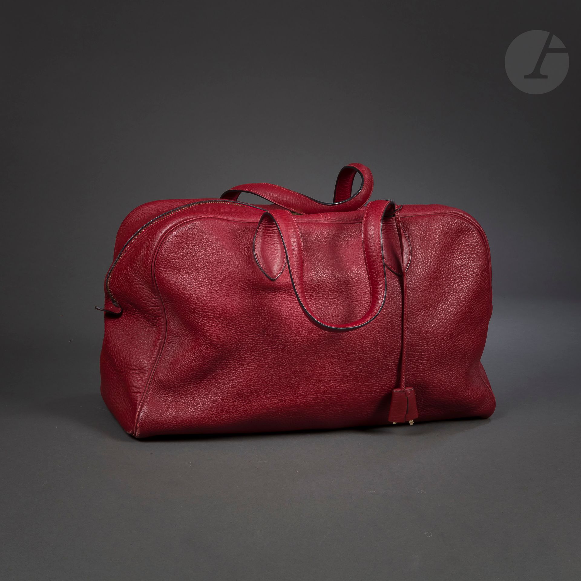 HERMES Paris Made in France
Sac Victoria en cuir grainé rouge, garniture en métal doré, cadenas et deux clés sous clochette, housse
43 x 20 x 25 cm (légères usures notamment au angles)