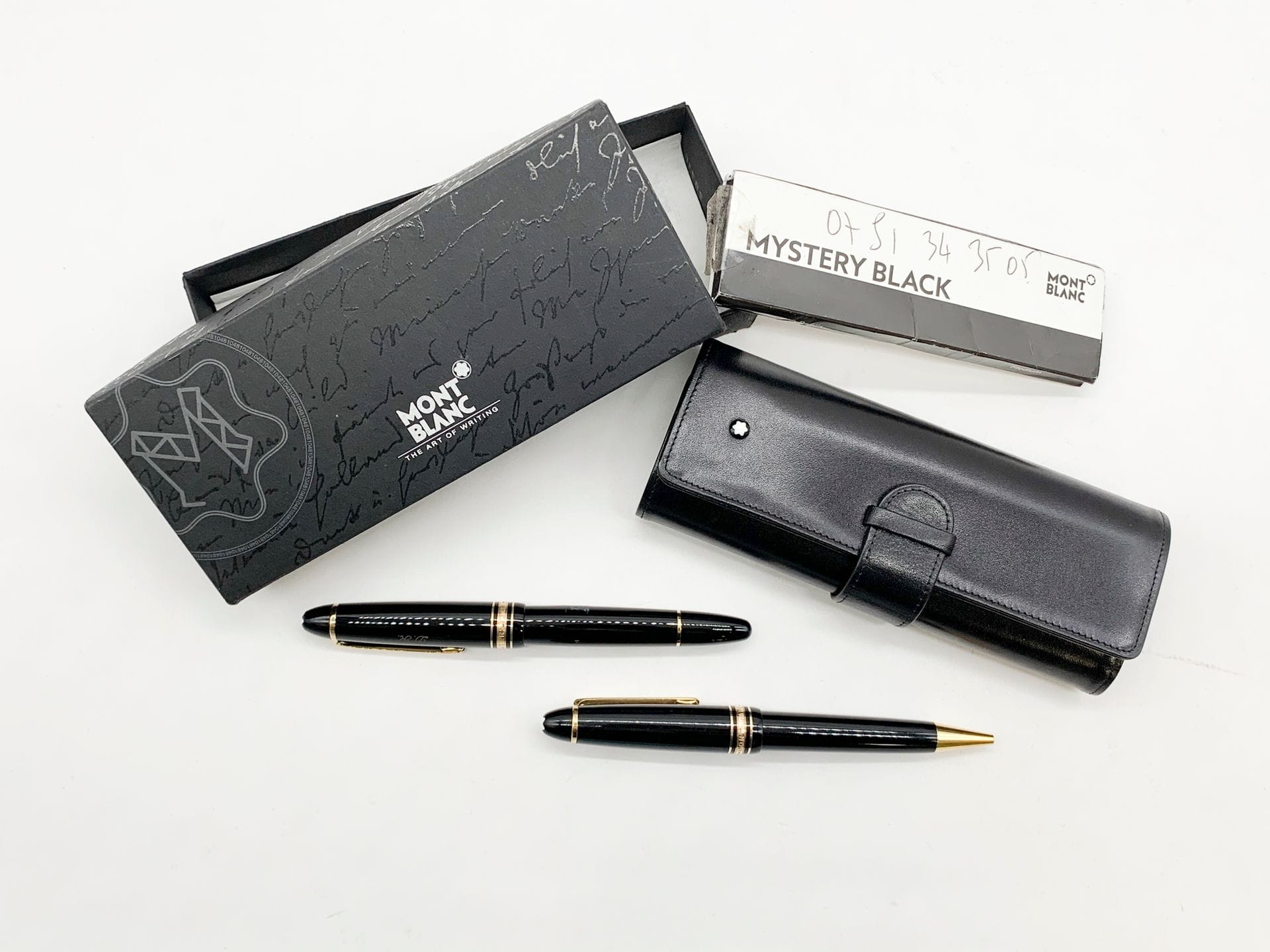 MONTBLANC 
Lot de deux stylos Meisterstuck en résine noire et métal doré comprenant un bille (et sa recharge) et un plume. Celui-ci accompagné de sa pochette en cuir noir, de sa boîte et de sa garantie