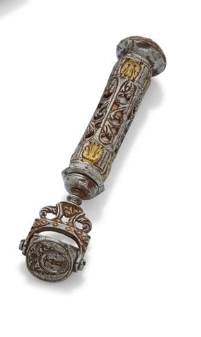 FRANCE  XVIIe SIÈCLE
Sceau à cacheter en fer forgé damasquiné de laiton, de section hexagonale, à décor ajouré, prolongé par un étrier maintenant un triple sceau rotatif gravé de deux armoiries. Il est surmonté d’un sablier en forme de dôme.
Hauteur : 12,5 cm