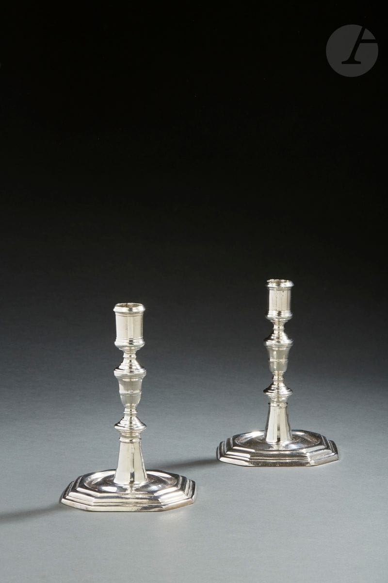 VITRÉ - FIN DU XVIIE DEUT DU XVIIIE SIECLE 
Paire de bougeoirs en argent uni à base carrée et huit pans coupés. Le fût, légèrement conique, se prolonge par un mouvement balustre rehaussé de joncs. Gravée au revers LL et SG.
Maître orfèvre : JEAN BERON RECU EN 1689 DECEDE EN 1728. 
Poids : 566 g - hauteur : 16,7 cm - base : 11,6 x 11,6 cm