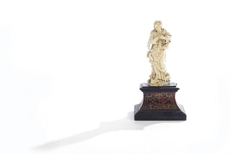 Sainte femme drapée surmontant un dragon en ivoire sculpté, la tête inclinée vers la gauche,  les bras croisés sur la poitrine. Ecole allemande du XVIIIe siècle. Socle en marqueterie Boulle. Manques. H : 15,8 cm.