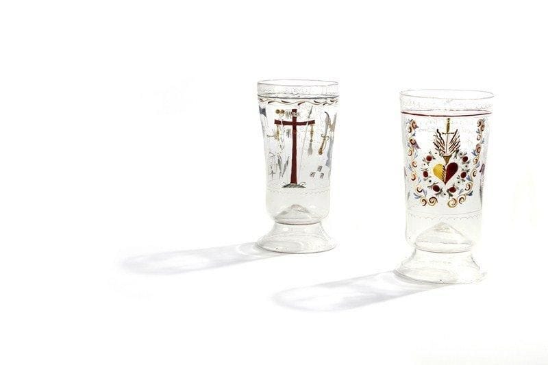 Paire de grands verres allemands décorés d'émaux du XVIIIe siècle. L'un de ces deux grands verres reposant sur des piédouches est daté de 1765. Tous deux sont décorés de dessins en émaux polychromes. Sur le premier les décors sont les instruments de la Passion, sur l'autre des rinceaux, des fleurs et le Sacré Coeur de Jésus. Bon état. H : 12 cm.