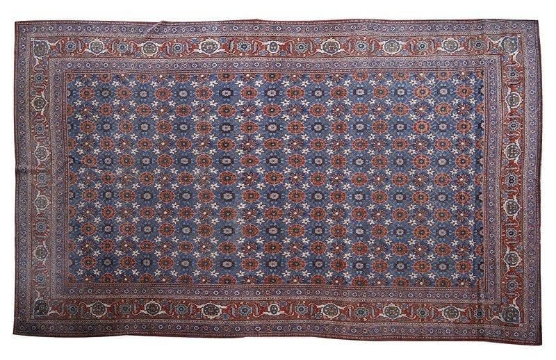 VERAMINE
Tapis à décor de rinceaux fleuris sur un fond bleu roi, large bordure rubis à guirlandes de fleurs entourées de deux galons bleus. 515 x 315 cm