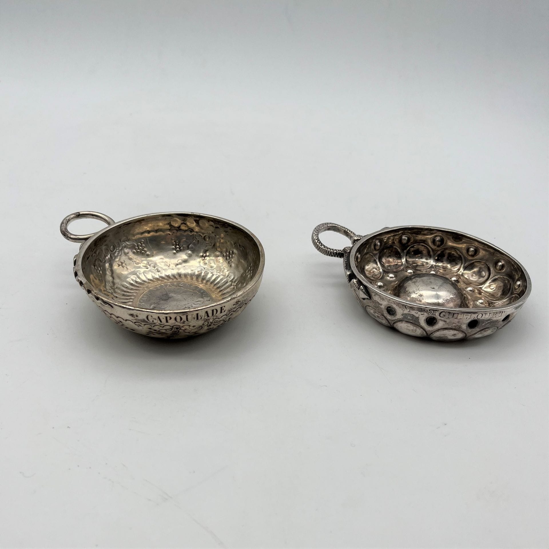 AURILLAC 1819 - 1838 ET PARIS 1782 - 1789
Deux tasses à vin en argent :
- PARIS : repoussée de cupules et de rangs de points, l'anse serpent ciselée d'écailles. Elle est gravée M TSE GUILLOUET.
Maître orfèvre : Denis COLOMBIER, reçu en 1776
Poids : 103 g
- Attribuée à AURILLAC et à l'orfèvre Guillaume LACAZE, son petit poinçon. Le fond reçoit une pièce aux armes d'Espagne datée de 1787, sur le pourtour est gravé le nom CAPOULADE, le décor est repoussé de canaux tors et de guirlandes fleuries.
Poids : 112 g  