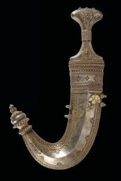 POIGNARD JAMBIYYA À LAME COURBE, YÉMEN, XIXE SIÈCLE Lame en acier damassé et monture en argent partiellement dorée, décorée de larges rosaces à cabochons en pâte de verre verte. Fourreau en argent partiellement doré, gravé de frises de petites feuilles et de rosettes, et agrémenté d'un couple d'oiseaux de part et d'autre d'une fleur à quatre pétales. Grosses bouterolles à corolles. L.: 33 cm