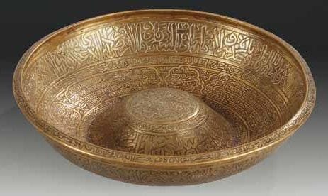 COUPELLE MÉDICINALE EN BRONZE, SYRIE OU JEZIREH, PROBABLEMENT XVIE SIÈCLE Coupelle à ombilic entièrement gravée de versets coraniques et d'inscriptions religieuses en caractères naskhi disposées dans des cartouches et des médaillons polylobés, ou en bandeaux superposés. Diam.: 20,5 cm Une coupelle réservée aux mêmes usages a été déposée au Quai Branly par le Musée National des Arts d'Afrique et d'Océanie, (inv. M.67.5.9) et reproduite dans le catalogue de l'exposition A l'ombre d'Avicenne. La medecine au temps des califes, Paris, IMA, 18 nov. 1996 au 2 mars 1997, n°188, p. 226. On en trouve également une dans la Aron Collection, reproduite dans James W. Allan, Metalwork of the Islamic World. The Aron Collection, Londres, 1986, n°21, p. 108-109