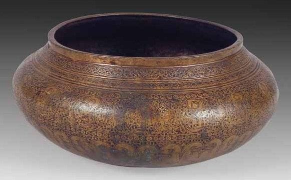 BASSIN TAS AUX MUSICIENS, EN LAITON, IRAN, ART ILKHANIDE, FIN XIIIE - DÉBUT XIVE SIÈCLE Bassin à base bombée, paroi convexe et ouverture cintrée, à décor gravé et traces d'incrustations en pâte noire. Paroi extérieure ceinturée par un large bandeau aux médaillons meublés de musiciens et personnages buvant sur fond de volutes de rinceaux, alternant avec de petites rosettes. Bandeau encadré en partie haute par des petites frises ornées de motifs tressés et de rinceaux foliés. En partie basse se déploie une frise de pendentifs lancéolés. A l'intérieur, ronde de poissons autour d'une rosace étoilée. Diam.: 19,5 cm et H.: 12 cm Provenance: Vente publique, Paris, A. Kevorkian-Me Boisgirard, 14 avril 1981, lot 107. Musiciens et personnages buvant appartiennent au répertoire iconographique classique des cycles princiers. Cependant, il est dans le cas présent tout à fait exceptionnel et nous n'en connaissons que de rares parallèles. Voir A.S. Melikian-Chirvani, Islamic Metalwork from the Iranian World 8th-18th centuries, Londres, 1982, n°75, p. 169-173
