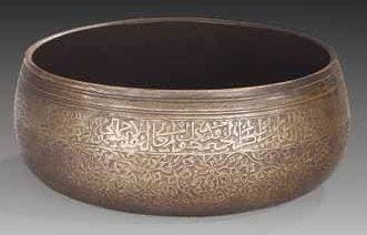 RARE BASSIN EN CUIVRE ÉTAMÉ, IRAN, ART TIMOURIDE, VERS 1500 Bassin à fond plat et panse bombée. Décor gravé sur la paroi extérieure d'un large bandeau de cartouches polylobés épigraphiés, alternant avec des quadrilobes aux rinceaux de palmettes et fleurons, formés d'un ruban continu. Sur la moitié inférieure, rinceaux d'agrafes, rosettes et lotus sur fond hachuré. Diam.: 27 cm et H.: 13,5 cm Les métaux timourides sont relativement rares et méconnus. Quelques pièces de cette époque sont cependant conservées au Victoria and Albert Museum, pièces dont le décor de rinceaux d'agrafes, rosettes et lotus peut être rapproché de celui visible sur ce bassin, voir A.S. Melikian-Chirvani, Islamic Metalwork from the Iranian World 8th-18th centuries, Londres, 1982, n°110, p. 250 et n°112, p. 254. On peut également comparer ce bol timouride à celui couvert, conservé dans une collection privée, et publié dans ce même ouvrage p. 242
