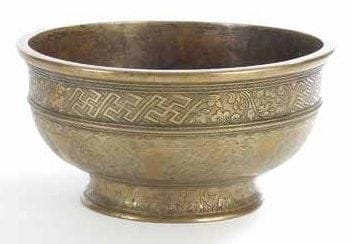 BASSIN EN BRONZE, INDE OU EUROPE XIXE SIÈCLE Bassin sur petit piédouche. Paroi extérieure à décor gravé de svastikas et rinceaux alternant dans des cartouches polylobés et en frises. Sur le pied, frise de palmes formant un une corolle, et sous la base, rosette rapportée. Diam.: 26 cm et H.: 14 cm