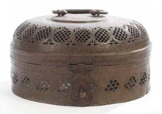 GRAND PORTE-TURBAN EN BRONZE, INDE, XVIIIE - XIXE SIÈCLE Boîte circulaire à couvercle, poignée et fermoir en lambrequin. Décor ciselé et ajouré en registres superposés de boteh à résille de quadrilobes. Dim.: 41 cm H.: 18,5 cm