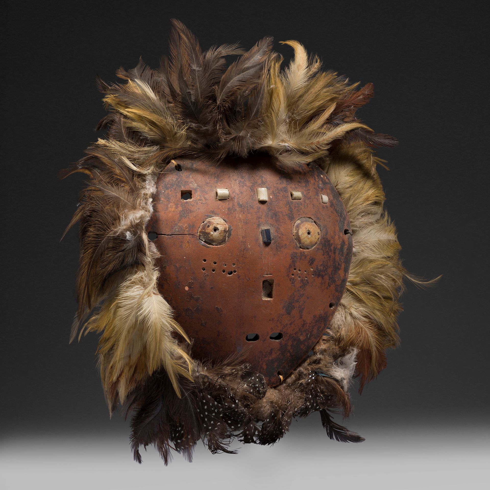 *Un très rare et ancien masque de la société du Bwami sculpté dans une calebasse, aux yeux, au nez et à la bouche faits d’incrustations lui conférant une présence à la fois naïve mais aussi bien vivante, et ayant conservé son ancienne corolle de plumes attachée par une tresse de fibres végétales. On connaît d’autres grands masques idimu de la société du Bwami qui était aussi entièrement cerclés de plumes tels que celui-ci, dont un provenant des anciennes collection Jeanne Walschot et Denise Schwob, ou un autre masque rare mais en cuir d’éléphant de l’ancienne collection Jeff Vanderstraete.

Pour le masque en cuir d’éléphant orné par des plumes du même type, voir : D. Biebuyck, Léga. Ethique et beauté au cœur de l’Afrique, Éd. KBC / Snoeck-Ducaju, 2002, p. 115 n° 60.

Léga, République Démocratique du Congo

Calebasse, perles, os, fibres végétales, plumes

H. : 17 cm sans les plumes



Provenance :

Collection Nadine Vinot-Postry, Cuernavaca.

 *Ce lot est vendu en importation temporaire.