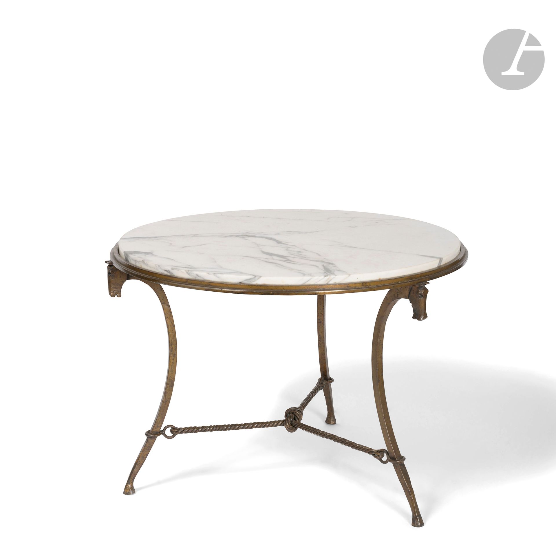 TRAVAIL NÉOCLASSIQUE DES ANNÉES 1940-50 DANS LE GOÛT DE JEAN-CHARLES MOREUX (1889-1956)
Têtes de chevaux & Cordelières
Table ronde de salon. La structure en fer battu et doré. Les trois jambages curvilignes à l’évocation de jambes de chevaux ; chacun reçu à la base par un sabot et terminé, en partie haute, par une tête de cheval stylisée. L’entretoise à la façon d’une cordelière. Le dessus en marbre veiné. H. 52 cm - D. 72 cm