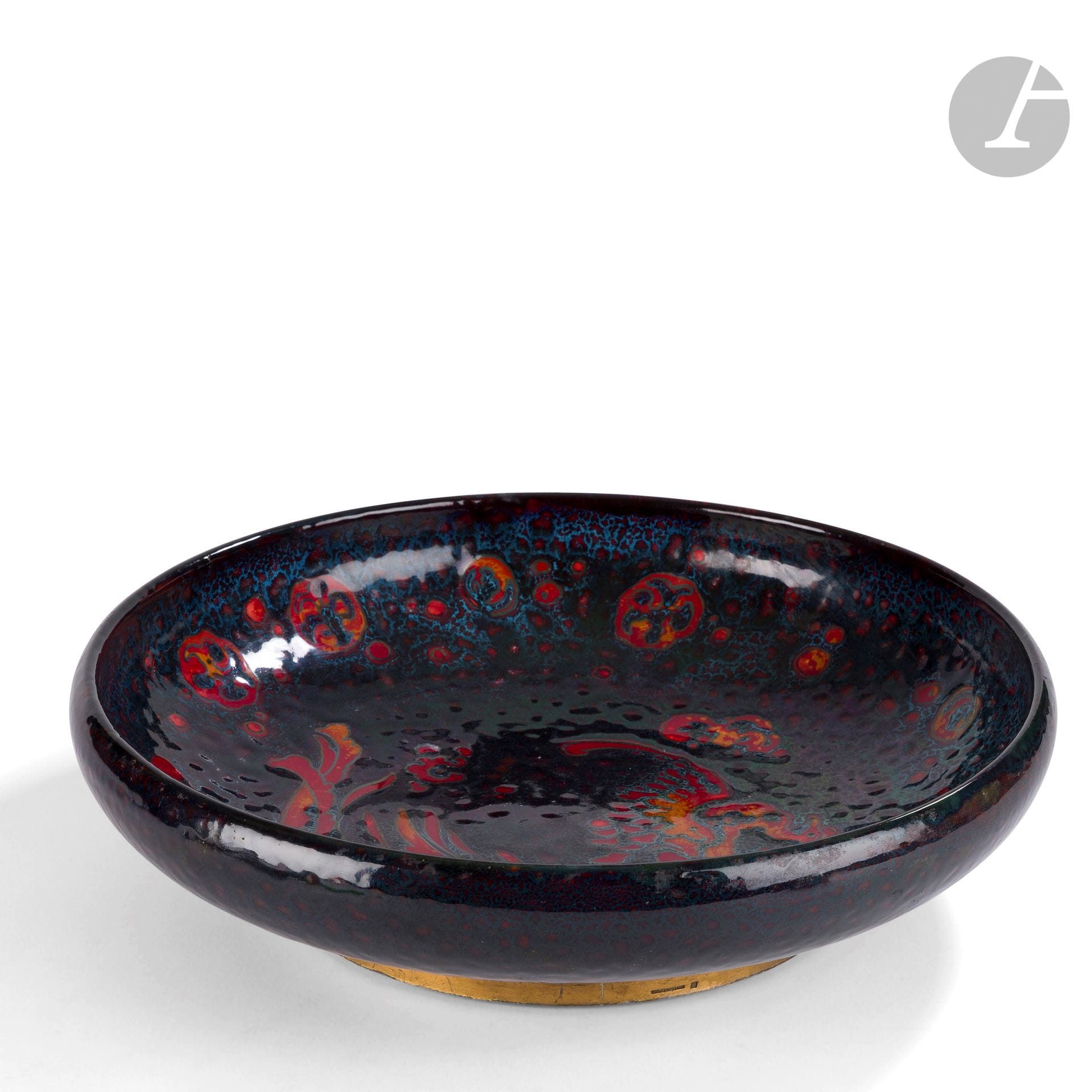 CHARLES JOHN NOKE (1858-1941) DIRECTEUR ARTISTIQUE - ROYAL DOULTON
Oiseau de feu, série Flambé
Très important plat creux. Épreuve en céramique émaillée polychrome ; l’oiseau titre traité rouge sur fond marbré et jaspé. Années 1920. Le talon cerclé de plomb doré, possiblement non d’origine. Long cheveu (stabilisé). Marqué du cachet ROYAL DOULTON et une étiquette ancienne lacunaire sous la base, porte une signature en partie masquée par le cerclage du talon. H. 10 cm – D. 37 cm