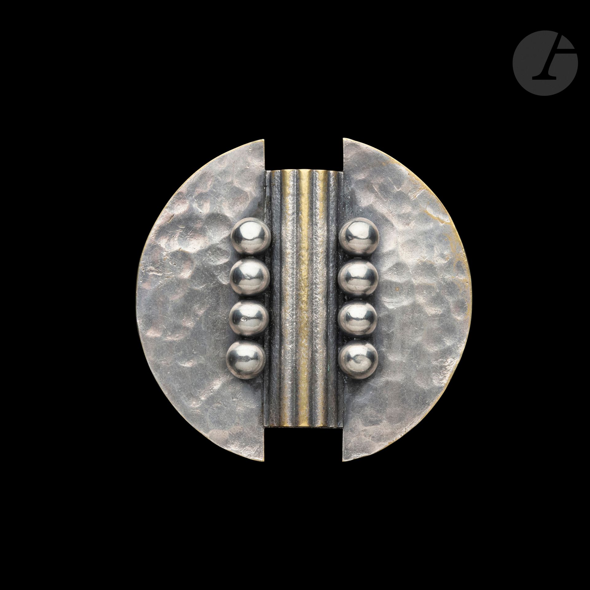 JEAN DESPRÉS (1889-1980)
Rare modernist brooch in silver plated metal. The circular plate with two indentations and entirely hammered surface receives, in its center, a fluted half-cylinder, evoking the corrugated sheet, framed by two rows of four large spheres treated smooth. Alterations to the silvering. Signed J. DESPRÉS at the tip and bears the hallmarks of Master Goldsmith and guarantee on the reverse. L. 6,8 cm

Provenance :
- Former Collection M. &amp; Mme F. (Thizy near Avallon - France), work acquired by them directly from the artist.
- Decorative arts and sculptures of the 20th century - Sale Ader-Nordmann-Dominique, Hôtel Drouot, June 2, 2017. Work presented under number 92 of the catalog.
- European private collection.