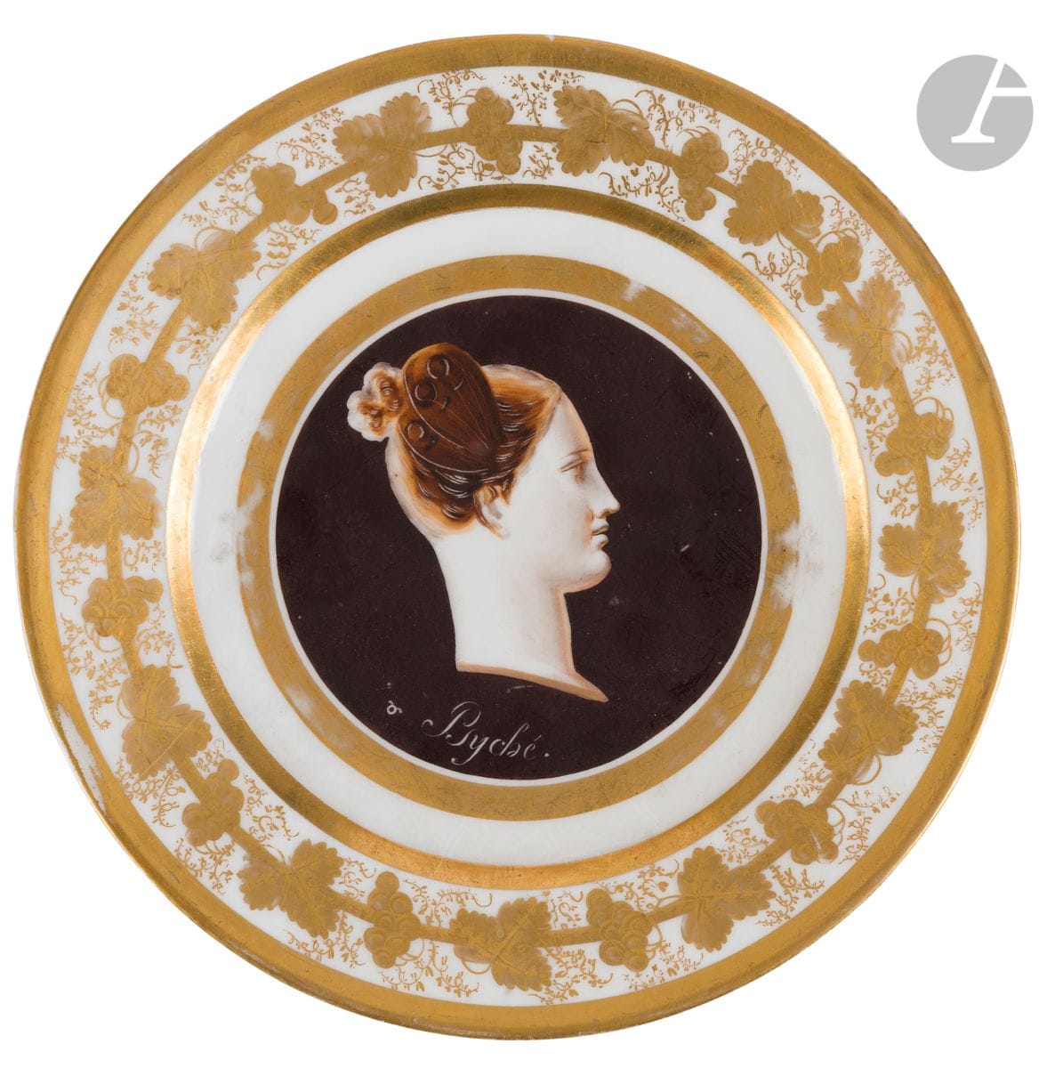 Paris
Assiette en porcelaine à décor façon camée d’un visage de Psyché de profil dans un médaillon à fond noir, l’aile décorée de feuilles de vigne en or.
Époque Restauration.
D : 22 cm
Quelques usures.