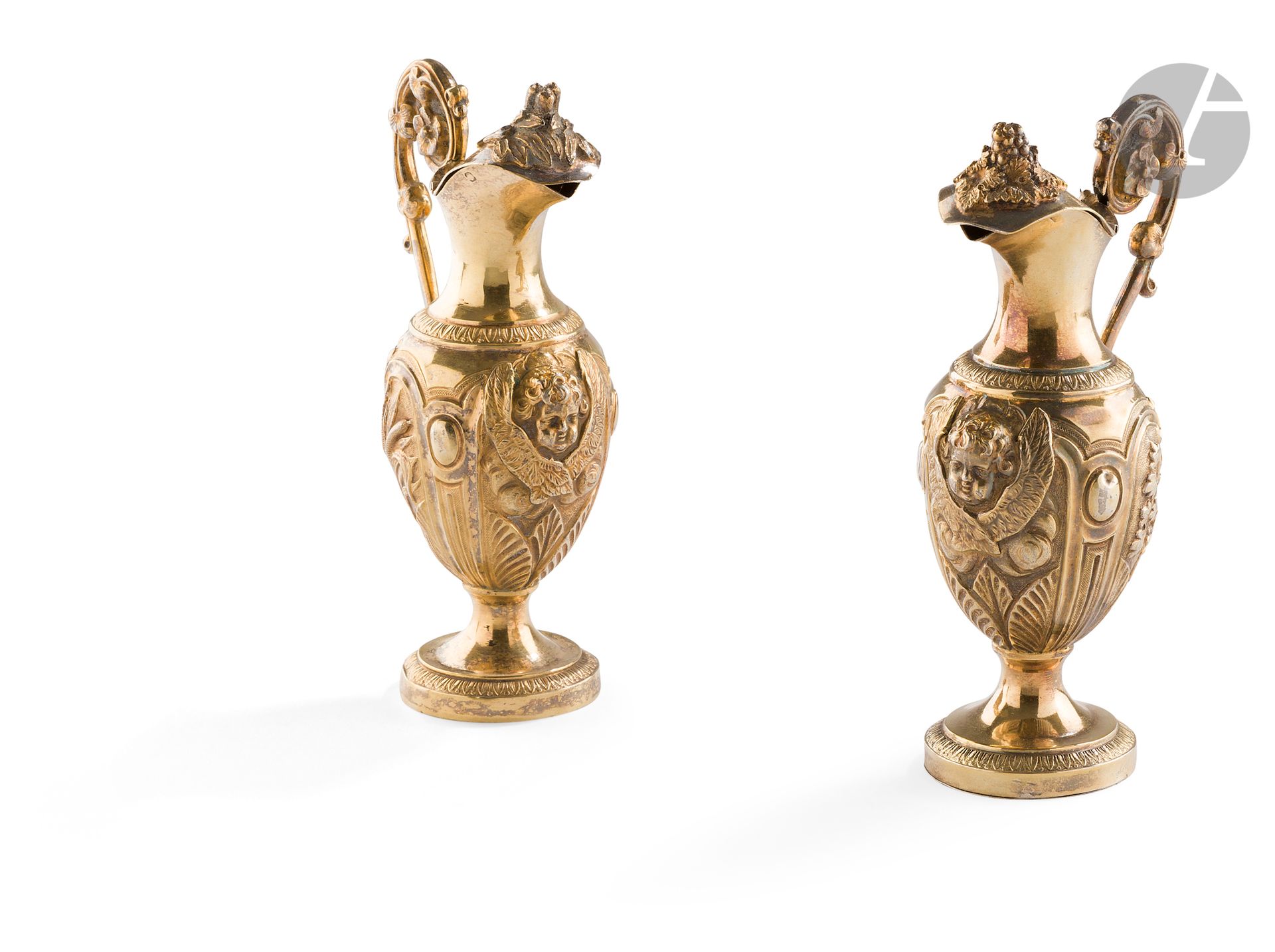 FRANCE XIXe SIÈCLE
Paire de burettes aux saintes huiles en argent doré de forme balustre. La base est rehaussée de palmettes sur fond amati en rappel au départ du col, le corps est repoussé de motifs de vigne pour l’une et de roseaux sur la seconde en rappel sur la prise. Anse latérale à enroulement. 
Poinçon minerve
Orfèvre : illisible
Poids : 228 g - hauteur : 15 cm
État : manque le plateau