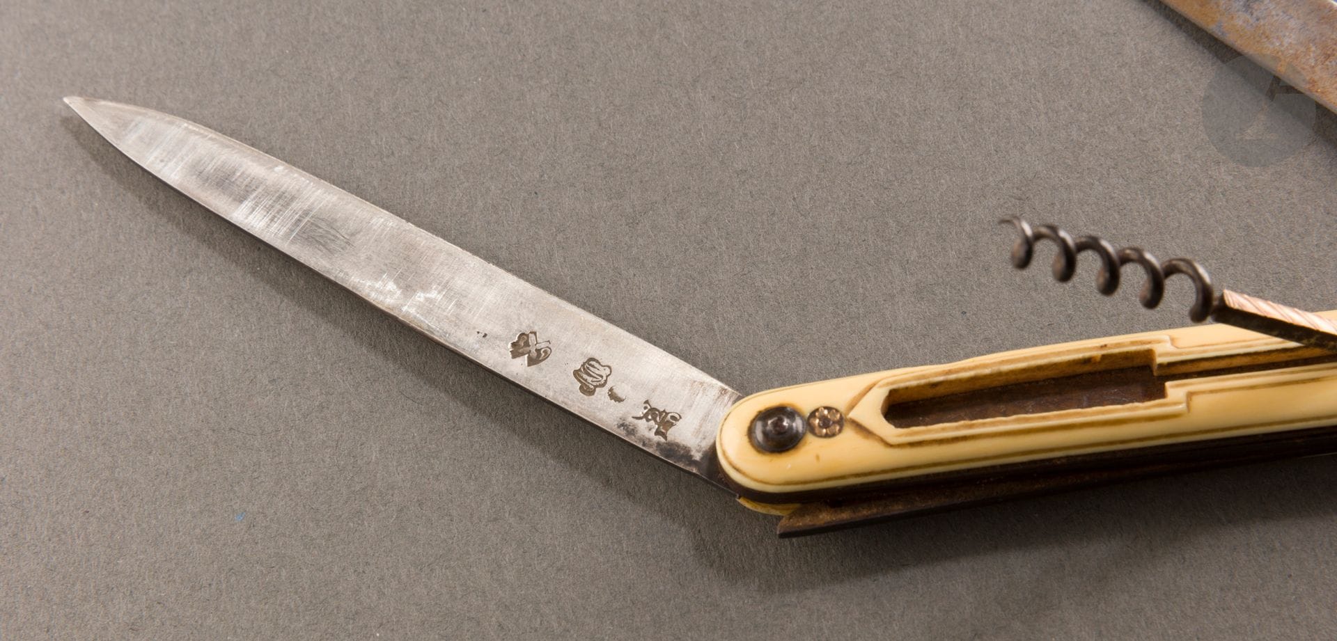 MILLS 1789 - JURISDICTION OF ORLÉANS - 
Folding knife/corkscrew with two silver and steel blades, with ivory plates and gold rosette rivets. The corkscrew opening to rocker is inserted in one of the ivory plates carved to the form. It is enhanced on the outer edge of a thin gold plate engraved with oblique nets.
Master cutler : Marin DEBANNE, from 1777
Hallmark : monogram OM (menus ouvrages) on the silver blade, the date 89 and on the steel blade : MAR(A ?)ND MOULINS and a stock
Gross weight : 25,5 g - length open : 31 cm, closed : 11,8 cm height of the corkscrew : 5 cm
Condition: two small cracks of use on each ivory plate