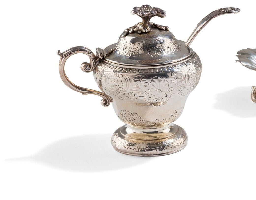 LONDRES 1780 ET 1785
Moutardier en argent, l’intérieur en verre bleu. Il pose sur un piédouche bordé de coquilles et de fleurs en rappel sur le corps balustre et le couvercle à dôme, à charnière, sommé d’une fleur sur son branchage. L’anse, à charnière, est terminée par des enroulements. La cuiller, de modèle filets coquille agrafes est gravée de la lettre N, datée de 1780.
Maître orfèvre : Paul STORR, reçu en 1784 pour le moutardier
Poids net : 231 g - hauteur : 11 cm