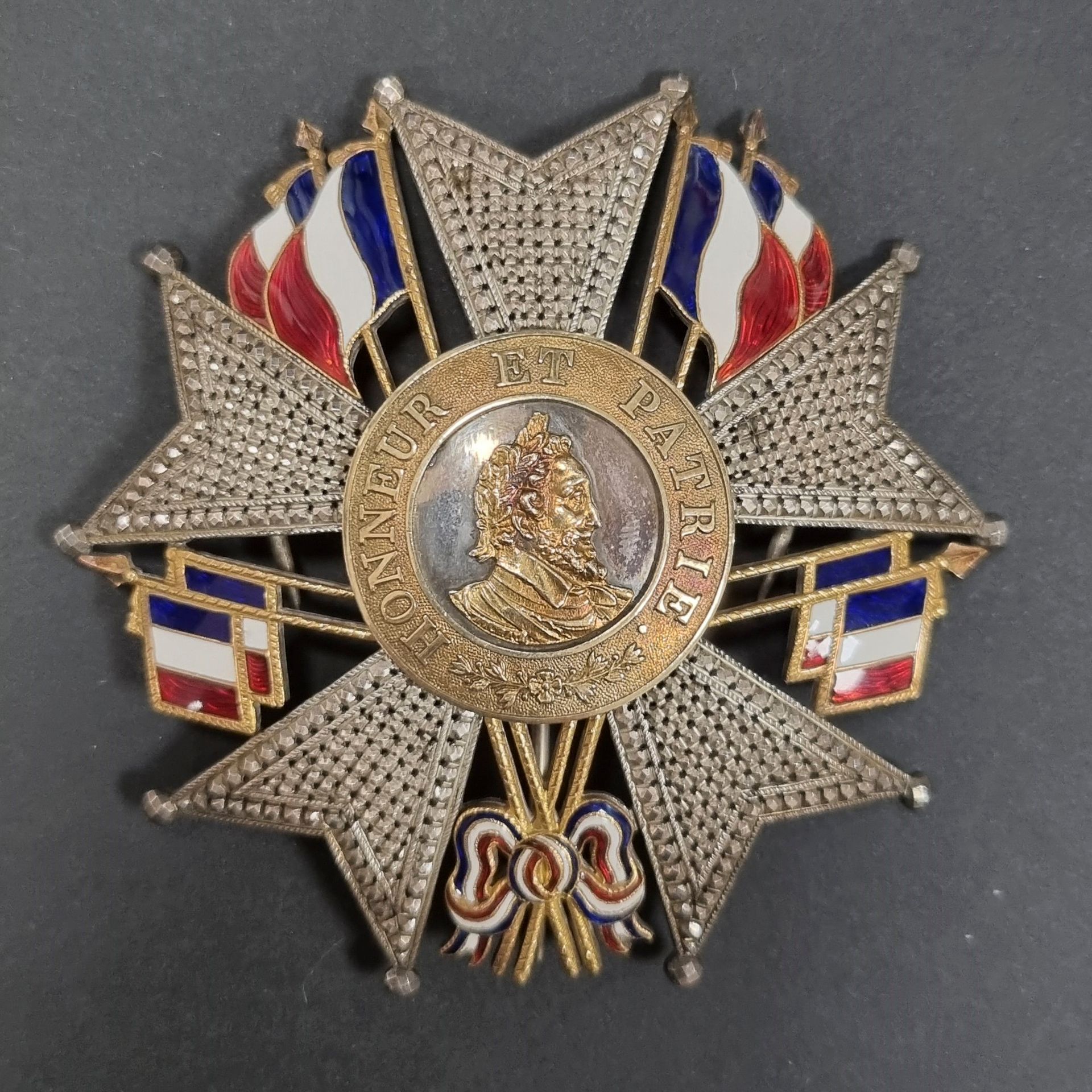 FRANCE 
ORDRE DE LA LÉGION D’HONNEUR (1802) 
Plaque métallique de grand officier ou de grand-croix, d’époque Monarchie de Juillet. 
En argent entièrement travaillé à pointes de diamant repercé. Entre chaque branche des drapeaux doublés d’or émaillé tricolore. Centre en argent, à profil d’Henri tête à droite et légende « HONNEUR ET PATRIE » sur fond grenu, en or. 
Revers à deux crochets et épingle basculante avec marque de « DASSIER BREVETÉ DU PRINCE ROYAL RUE DE RICHELIEU 12 – PARIS ». 
Poinçon tête de sanglier sur le crochet.
82 mm - Poids brut : 37 g
Dans son écrin hexagonal recouvert de maroquin vert, gainé de soie et velours ivoire. 
T.T.B.

Dassier : fabricant d’équipements militaires et fournisseur d’ordres de chevalerie à la fin de la Restauration et sous la monarchie de Juillet. 
Une plaque ayant appartenu au Duc d’Aumale (diamètre 75 mm) portant sa marque 
« DASSIER, Chapelier passementier, breveté de S.A.R Monsgr le duc d’Orléans, à Paris, rue de Richelieu, n°12 » dans les collections de Chantilly.