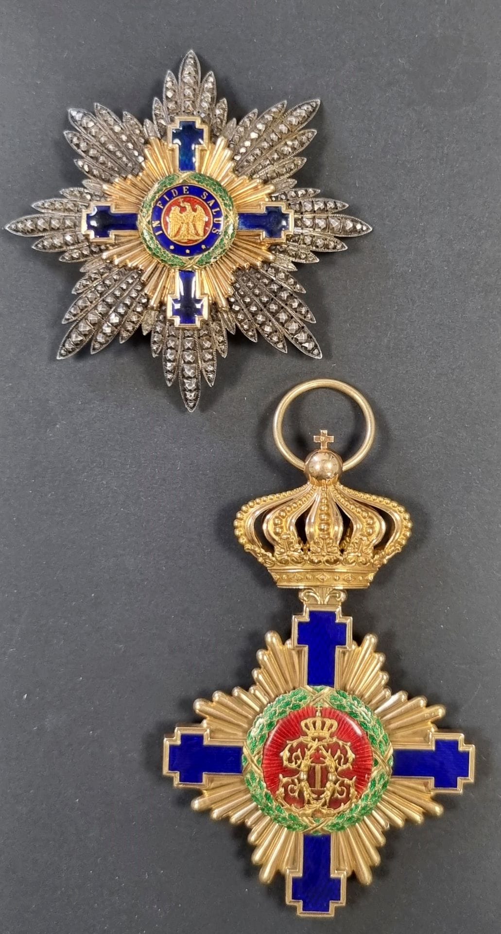 ROUMANIE
ORDRE DE L’ÉTOILE DE ROUMANIE (1877
Ensemble de grand-croix du 1er type, luxueuse fabrication française comprenant :
- Important bijou en or creux et émail (éclats à la légende à l’avers). Poinçon tête de Mercure, pour petits ouvrages à l’export (avant 1879), et traces de poinçon d’orfèvre aux bâtons entrecroisés (probablement Kretly).
110 x 71 mm. Poids brut : 48 g.
Poinçon
B à T.B.
- Plaque.
En argent travaillé à pointes de diamant, repercé. Croix centrale en or émaillé (petits défauts, éclats et restaurations). Revers à épingle basculante et deux crochets, avec marque du fabricant « N°46 KRETLY PALAIS ROYAL PARIS » Diam : 84 mm
Poids brut : 60 g
T.T.B. (Coup à une pointe), vers 1877.

Historique : 
Les insignes en or de l’ordre de l’étoile de Roumanie de fabrication Kretly sont particulièrement rares. Ils correspondent soit à la première commande des insignes de l’ordre de l’Étoile (faite à Kretly en 1877), mais plus probablement à la commande faite pour l’éphémère ordre de l’Union qui précède l’ordre de l’Étoile (et qui possédait des insignes en or comme ici) et modifiée par la suite. Le pontet du bijou correspond à celui de l’ordre de l’Union.

Nous remercions Monsieur Jean Luc GUITERA de son aide.