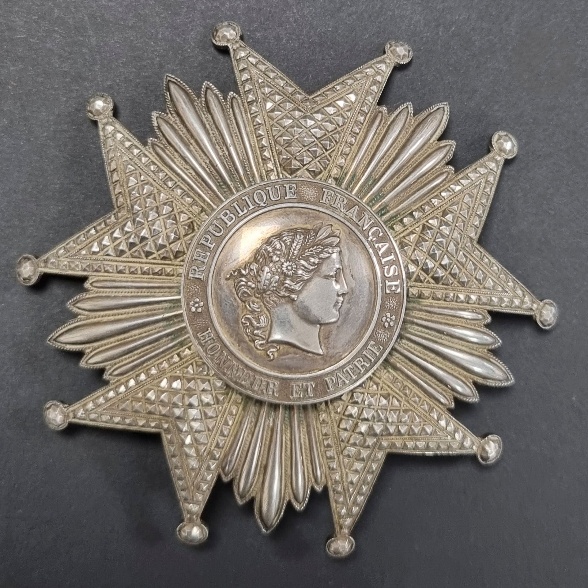 FRANCE 
ORDRE DE LA LEGION D’HONNEUR (1802).
Plaque de grand-croix d’époque IVe République. 
En argent, à branches travaillées à pointe de diamant. Centre en plusieurs parties.
Revers à attache basculante et deux crochets. Poinçon tête de sanglier et d’orfèvre (probablement la Maison Arthus Bertrand).
94 mm - Poids net : 101 g 
T.T.B.