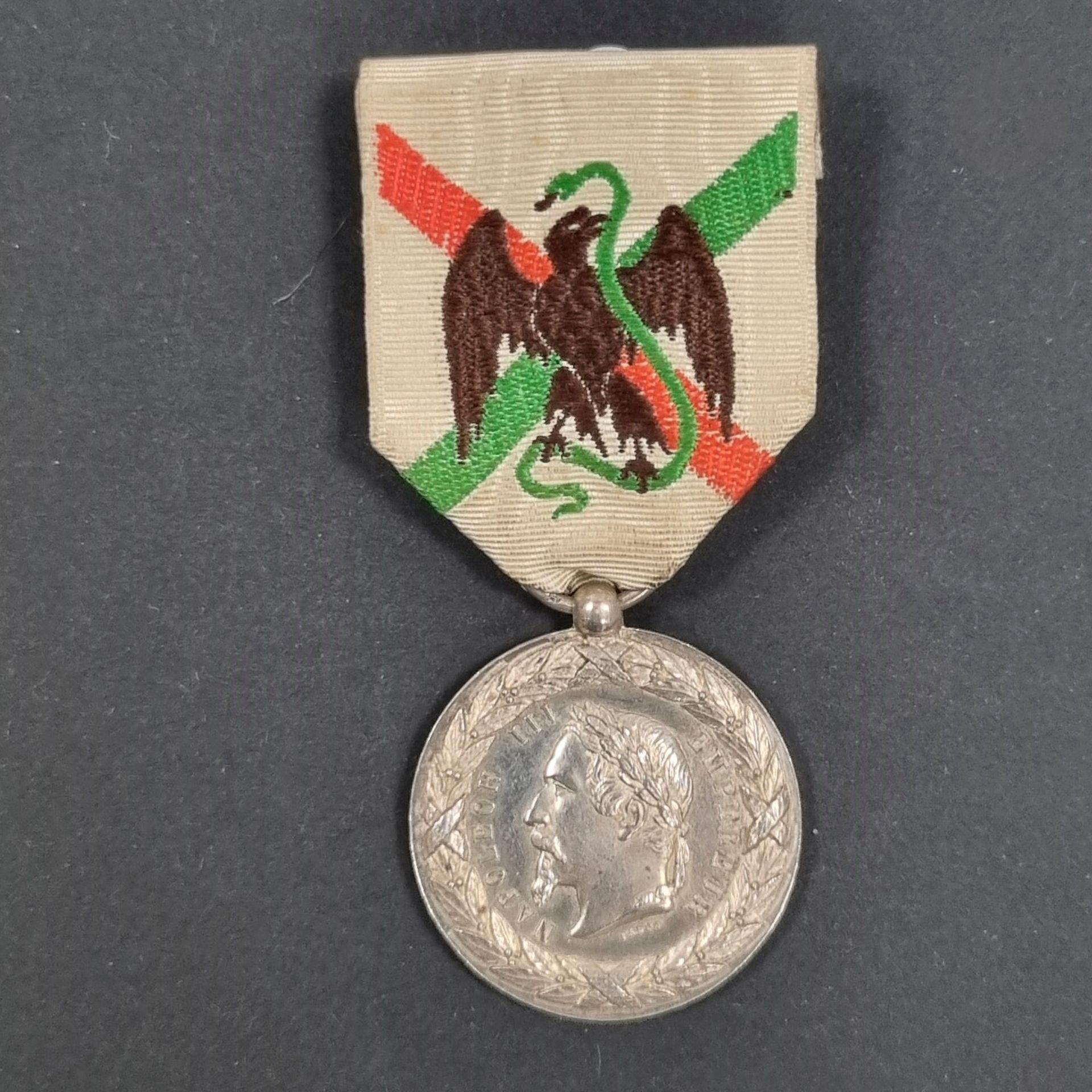 FRANCE 
Médaille de la Campagne du Mexique, signée FALOT.
En argent. Ruban. Poinçon tête de sanglier. 
Bélière boule. Anneau postérieur poinçonné de Chobillon. 
30 mm - Poids net : 13,9 g 
T.T.B.