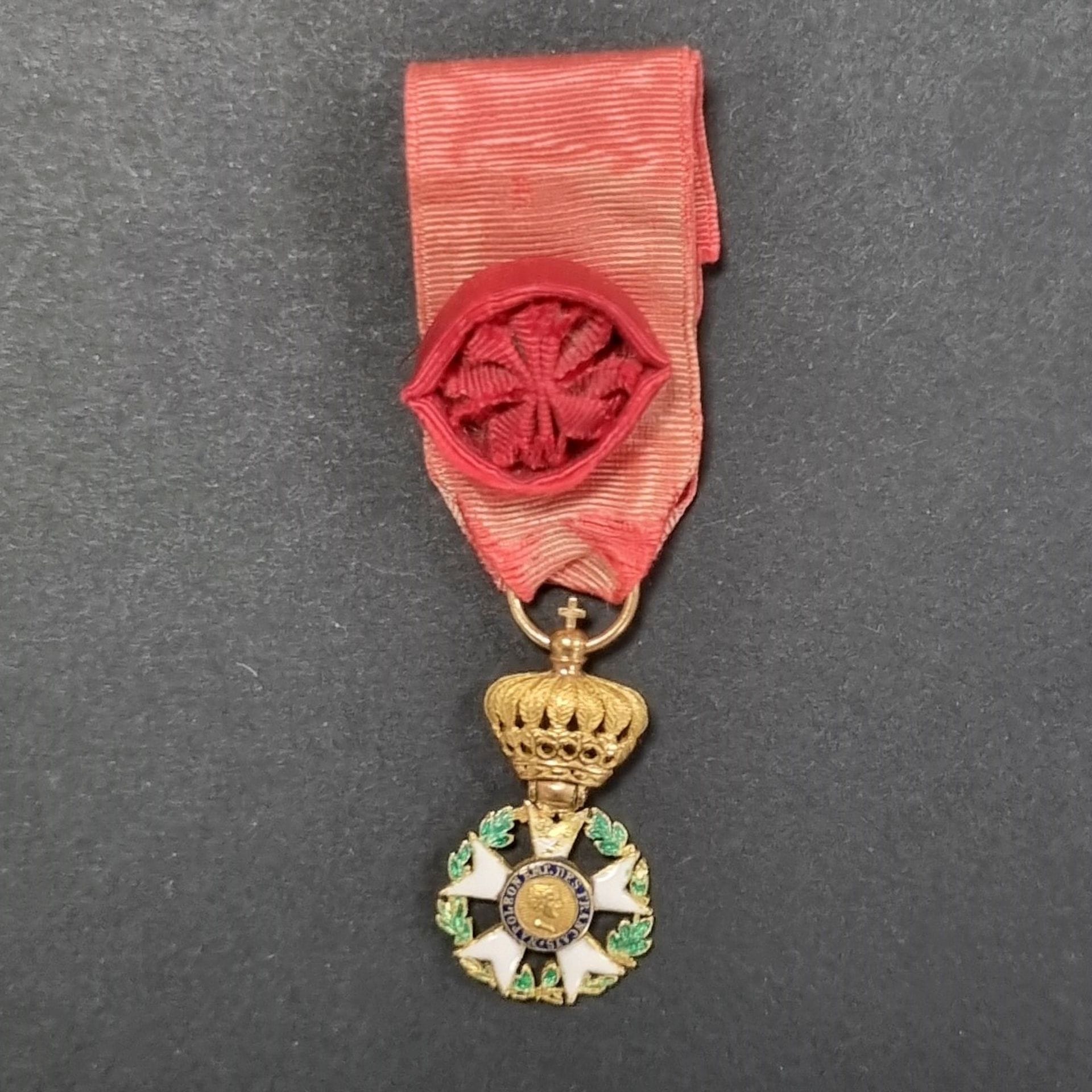 FRANCE 
ORDRE DE LA LEGION D’HONNEUR (1802).
Aigle d’or du 2e type, à couronne montée à charnière, en miniature. 
En or et émail (éclats et manques à la branche supérieure). Importante couronne à douze branches à décor de feuillages et palmettes. 
Ruban à rosette ancien postérieur. 
25 x 14 mm - Poids brut : 2,9 g 
T.B.