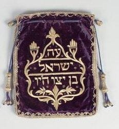 Sac à tefillin. Velours bleu brodé de fils métalliques dorés. Important décor central de Hemsa et d'inscriptions hébraïques au nom du propriétaire. Glands de passementerie (usures et fentes au velours).Afrique du Nord. XIXe-XXe siècle. Modèle plus ancien et plus rare que le précédent. 27 x 21,5 cm