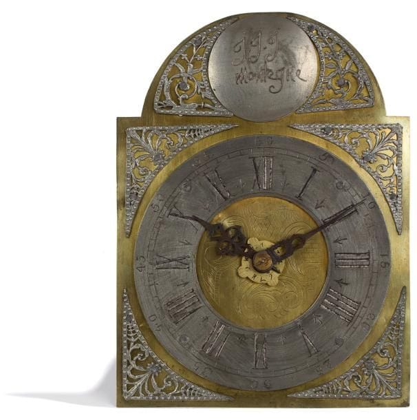 Horloge du Nord-Est à cadran en étain et écoinçons sur plaque gravée au centre. Le sommet en demi-lune porte un disque gravé : "J.J.J Montegne". Mouvement journalier à échappement à ancre à réveil matin seul. Dispositif à pointes et crochet pour fixer l'ensemble sur le mur. Récemment restaurée. (Manque le balancier ; avec ses poids et contre-poids issus de la restauration). XVIIIe siècle. Haut. : 32,5 cm - Larg. : 24 cm - Prof. : 14 cm.