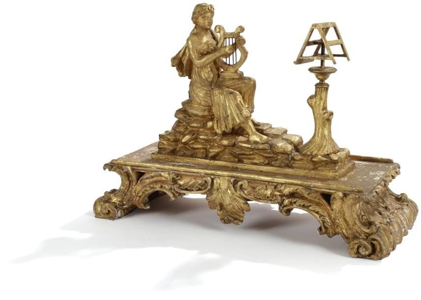 Groupe en bois sculpté et doré représentant une jeune femme jouant de la lyre devant un pupitre à musique. Base rocaille à décor de feuilles d'acanthe stylisées. Italie, XVIIIe siècle. Reprise à la dorure, renforts et petits manques. Haut. : 37 cm - Larg. : 51 cm - Prof. : 24 cm.