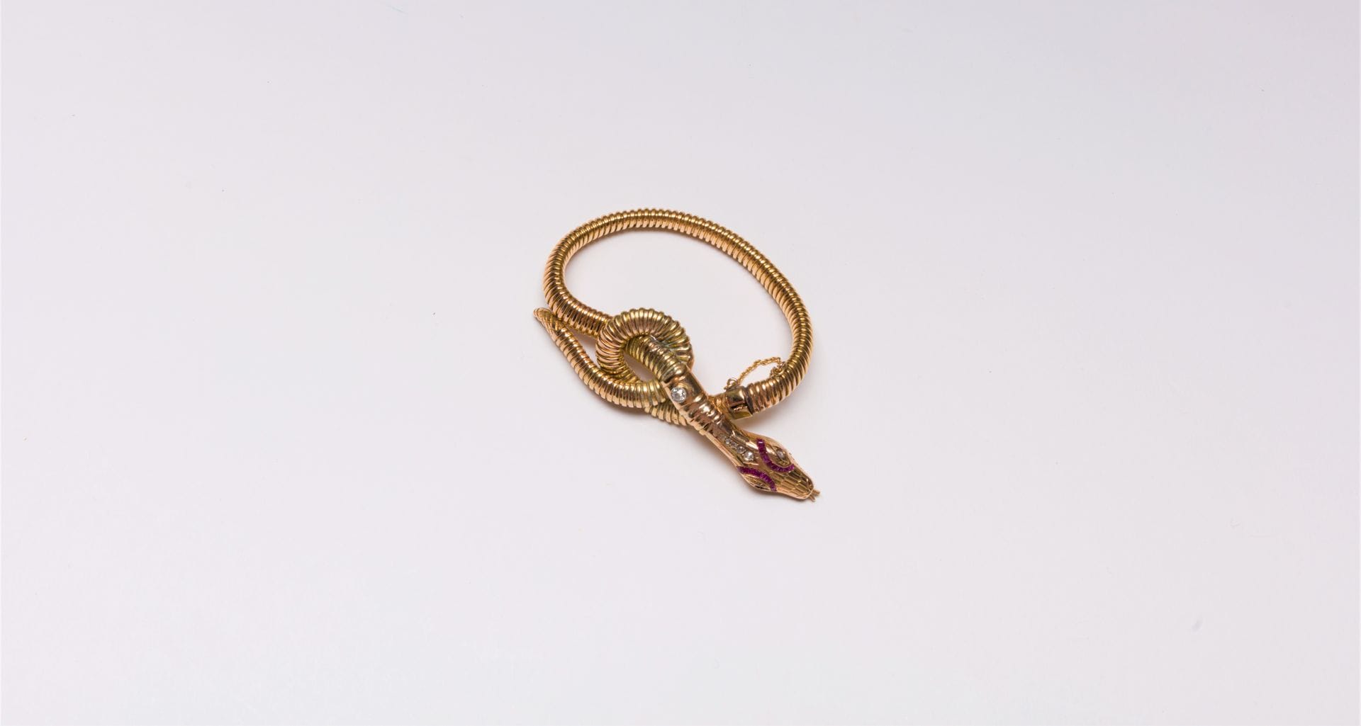 Bracelet tubogas en or 14K (585) formant un serpent, la tête et les yeux piqués de diamants taillés en roses, soulignés de rubis calibrés, le corps orné d'un diamant de taille ancienne. 
Largeur : 15 cm environ. Poids brut : 21,2 g (manque, réparations, chocs)