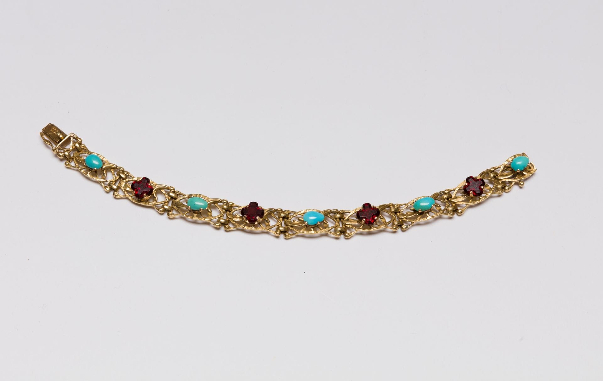 Bracelet articulé en or 18K (750), les maillons ajourés et ciselés de feuillages agrémentés de turquoises cabochons ou de grenats quadrilobés. Travail français de la fin du XIXe siècle. Longueur : 19 cm environ. Poids brut : 26,6 g