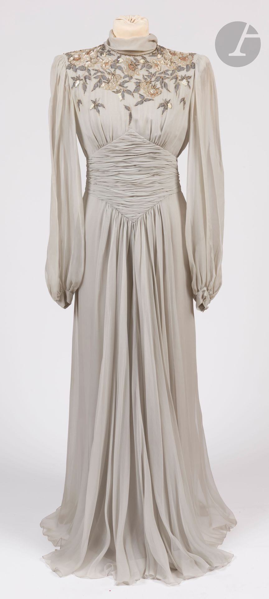 Jean-Louis SCHERRER Haute Couture, années 1980
Robe longue en mousseline gris clair, plissée à la taille et brodée de perles et paillettes des épaules à la poitrine, écharpe intégrée (auréoles sous les bras et quelques petites taches)
Taille pouvant correspondre à un 34-36 environ