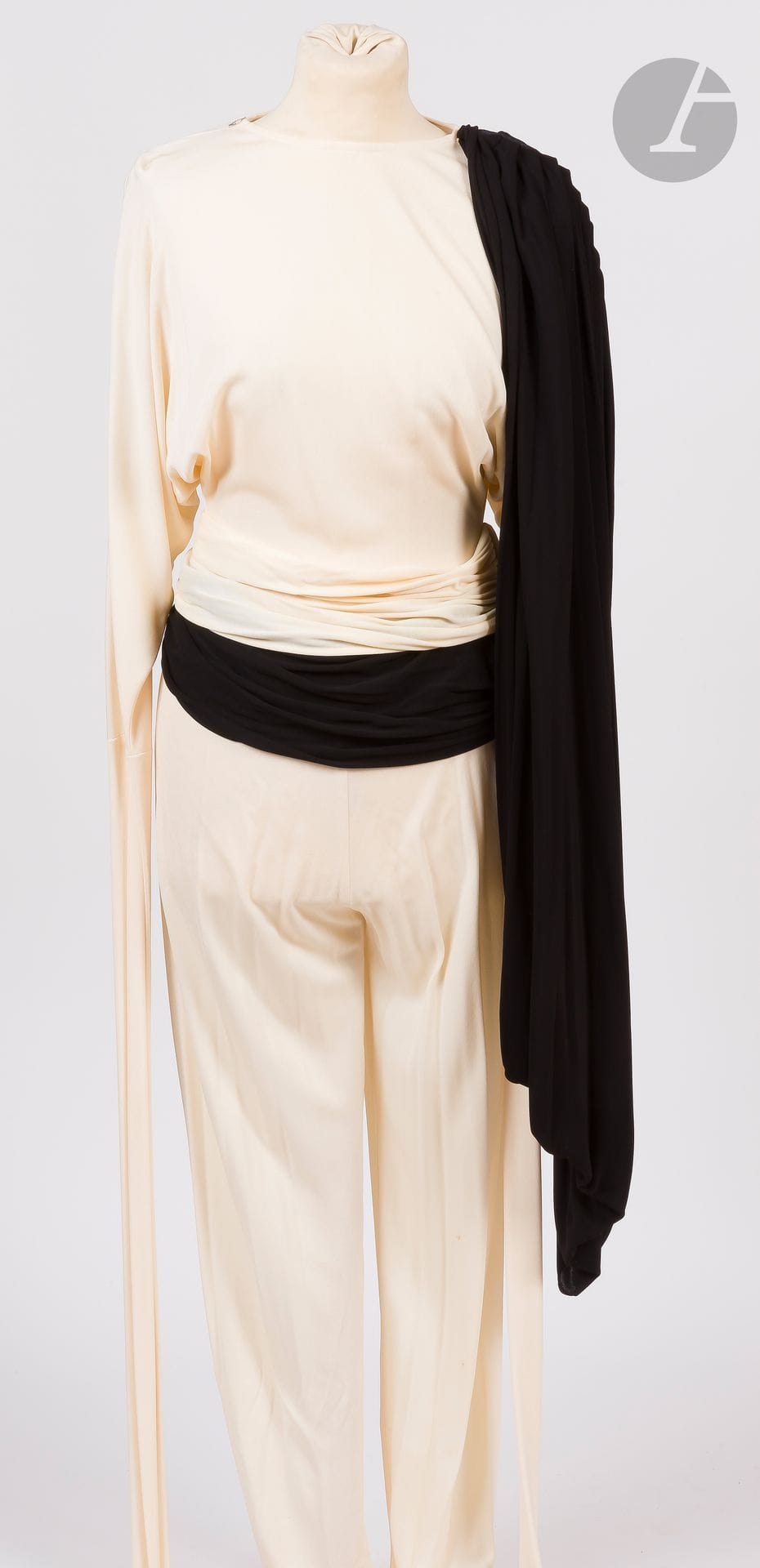 OMO Norma KAMALI, 1980s
Cream crepe trouser jumpsuit with very long batwing sleeves, matching belt, a single removable draped shoulder panel and another black crepe belt (small stains).
Size may correspond to a 34-36 approx.
