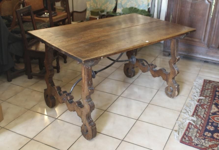 Table en noyer aux deux pieds en lyre. Espagne XVIIe siècle. Ils sont reliés au plateau par deux entretoises en fer forgé comportant un disque médian en partie centrale. Petite réparation sur l'un des pieds en partie haute. H: 75 cm - L: 136 cm - P: 85 cm.