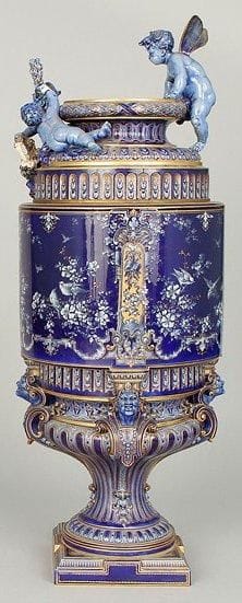 SEVRES
Grand vase rouleau sur piédouche carré muni à l'épaulement et au col de deux enfants chérubins portant une couronne de fleurs, dont un ailé. Décor dans le goût de la Renaissance, de pâte sur pâte sur fond bleu lapis, en quatre compartiments d'oiseaux branchés. Godrons à fond or au piédouche et à l'épaulement. Le piédouche repose sur quatre têtes de mascarons. Marqué: "1886-1887". XIXe siècle. H: 53,5 cm. Petits manques à la couronne de fleurs. Une aile manquante.