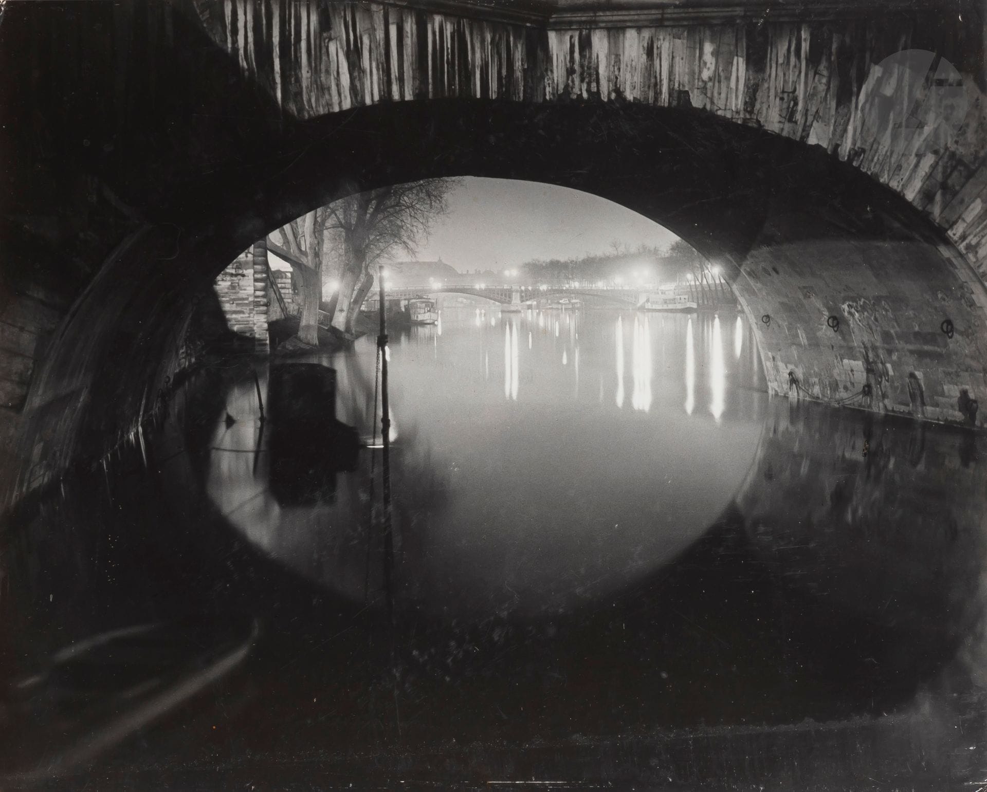 Brassaï (Gyula Halász, dit) (1899-1984)
Pont Royal. Paris, c. 1930.
Épreuve argentique d’époque, contrecollée sur isorel.
39 x 48,5 cm

Bibliographie :
Brassaï, Paris de nuit, Paris, Arts et métiers graphiques, 1933, p. 19.

« L’éclat d’un lampadaire met en valeur les pierres du pont Royal mordues et délavées par la pluie. » (Paris de nuit).
