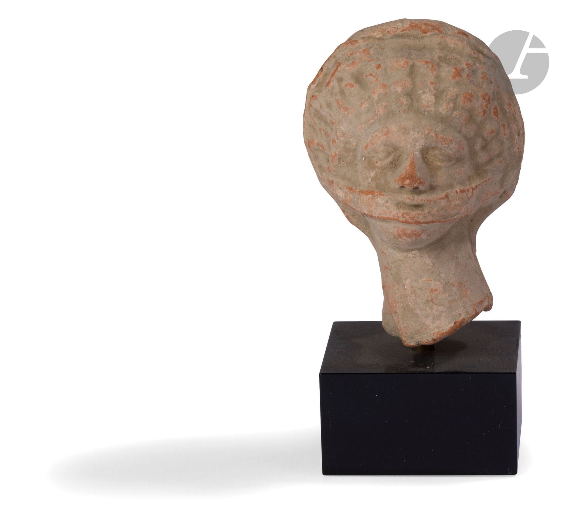 Tête féminine à la coiffure en diadème bouclée, un ruban lui couvre la bouche 
Terre cuite.
Art grec, IV-IIIe siècle avant J.-C. 
Hauteur : 6 cm

A Hellenistic Terracotta Head of a Woman, 4th - 3rd Century BC