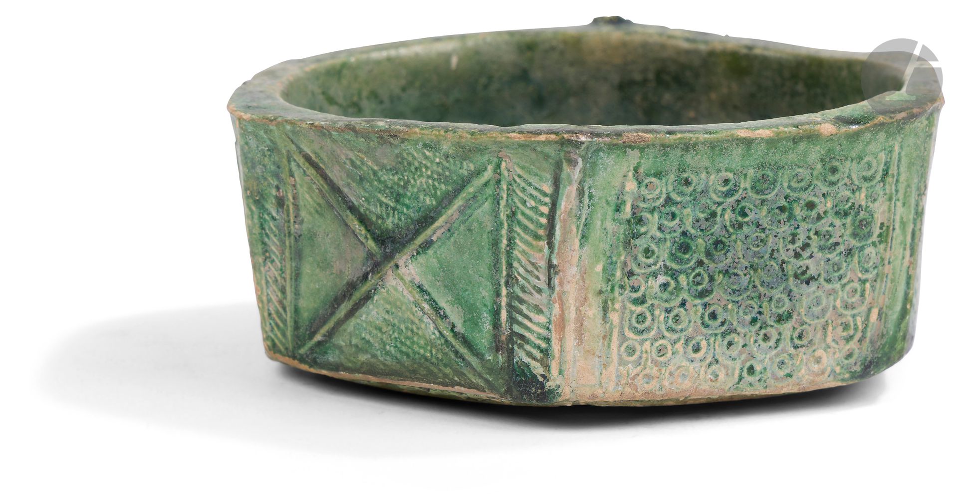 Petit bol à décor géométrique, Iran ou Proche-Orient, VIIIe - Xe siècle
Petit bol à pans coupés et coupe hexagonale en céramique argileuse à décor moulé et estampé sous glaçure verte de croix alternant avec des registres écaillés. 
Diamètre max. : 10,1 cm
Quelques sauts de glaçure, irisation et encrassement.

La forme spéciale de ce petit bol semble s’inspirer des productions de métal.
Les deux lots 171 et 172 sont représentatifs des premières productions céramiques glaçurées des débuts de l’Islam. Elles semblent avoir été en vogue à la période omeyyade pour disparaître au début de l’ère abbasside (cf. WATSON, Oliver, Ceramics from Islamic Lands, Kuwait National Museum, Al-Sabah Collection, Thames & Hudson, London : 2004, p. 157).
Comparaisons : Les bols MAO S 374 et S 784 du Musée du Louvre de Paris réalisés avec la même technique, retrouvés dans les fouilles de Suse en Iran et attribués aux VIIIe - Xe siècles. 

A Monochrome Hexagonal Pottery Bowl, Iran or Near-East, 8th - 10th Century