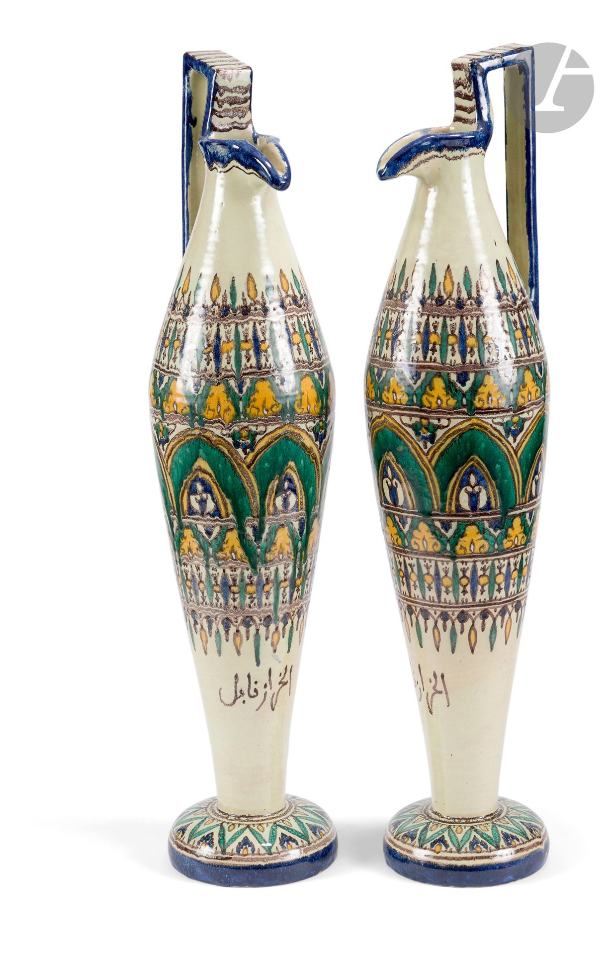 Paire de hautes aiguières chianti, Tunisie, Nabeul, atelier El-Kharraz, vers 1920-40
Verseuses à panse fusiforme sur piédouche convexe, la lèvre pincée et l’anse angulaire. En faïence à décor légèrement fusant d’arcatures vertes abritant des fleurons et encadrées de frises végétales et géométriques. L’anse striée de brun, le pied à décor de ligne brisée verte. Inscription en arabe sur la partie inférieure de la panse « El-Kharraz Nabeul » et estampille sous la base de l’une. 
Hauteur : 70 cm 
Éclat sur un pied.

A Pair of Tall Pottery Ewers Chianti, Tunisia, Nabeul, El-Kharraz Factory, c. 1920-40