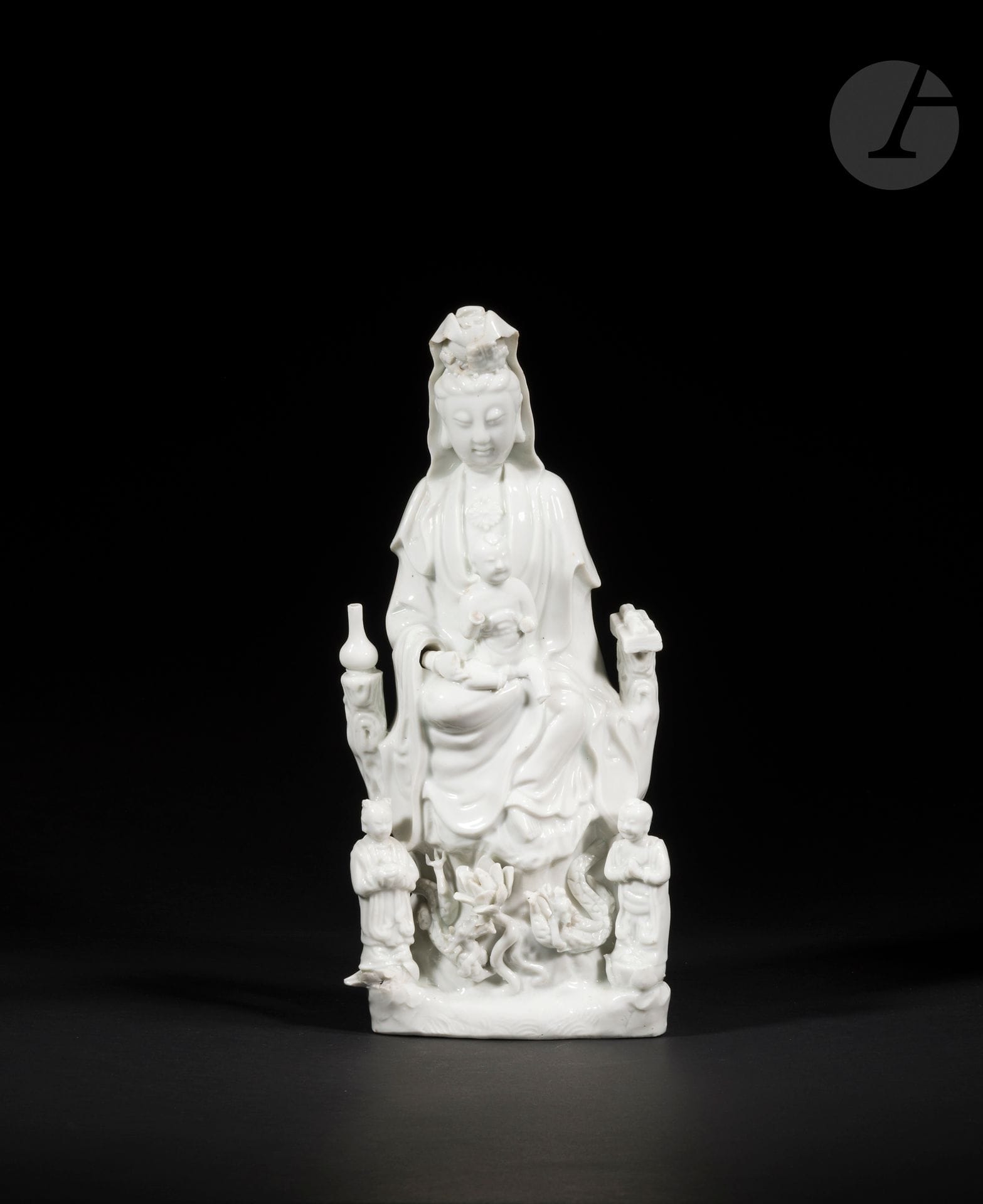 Large Chinese white porcelain Guanyin, China, Dehua, 18th century
Depicted seated holding a child, right leg bent and left leg dangling in a position known as vāmārdhaparyaṅka. A lustral water bottle to her right rests on one side of her throne, a scroll and sutra books to her left. At his feet, his two acolytes LongNü, holding the Pearl of Light and ShanCai TonZi, hands in adoration. Between them, on a terrace, a lotus flower surrounded by two facing dragons.
Height: 36.3 cm
Minor accidents.

ShanCai TongZi, 善財童子, "the child of wealth" and LongNü, 龍女, "the dragon's daughter", appear in Buddhist and Taoist folk tales as servants of GuanYin, 觀音菩薩. Their depiction was probably influenced by that of the "Jade Lady", 玉女, and that of the "Golden Child", 金僮, both of which appear in the iconography of the "Jade Emperor", 玉皇大帝.
